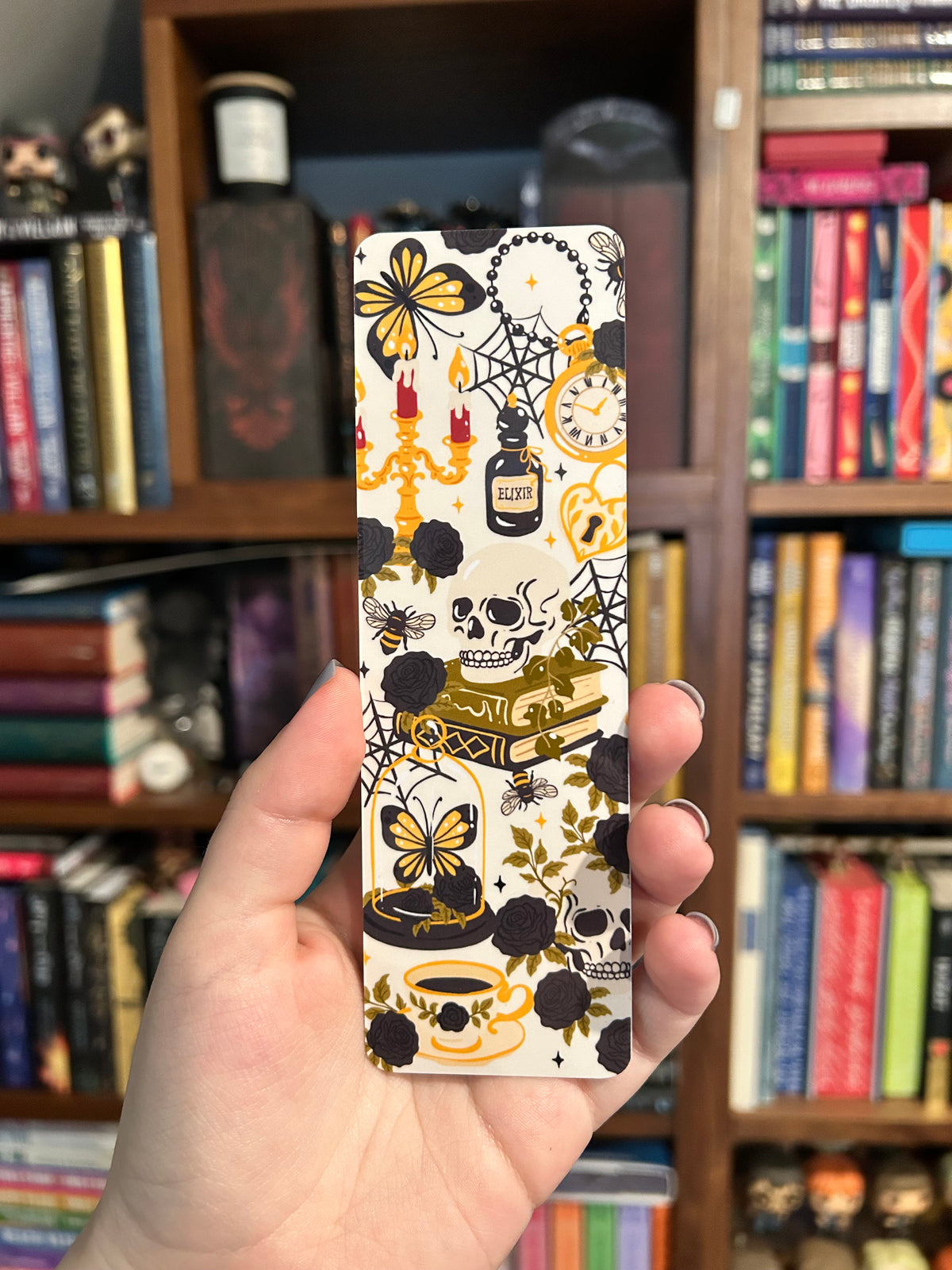 Double-sided gothic bookmark with skulls, black roses, candles, potion bottles, and golden accents on a cream background, paired with a black reverse featuring cream spiderwebs and golden bees.