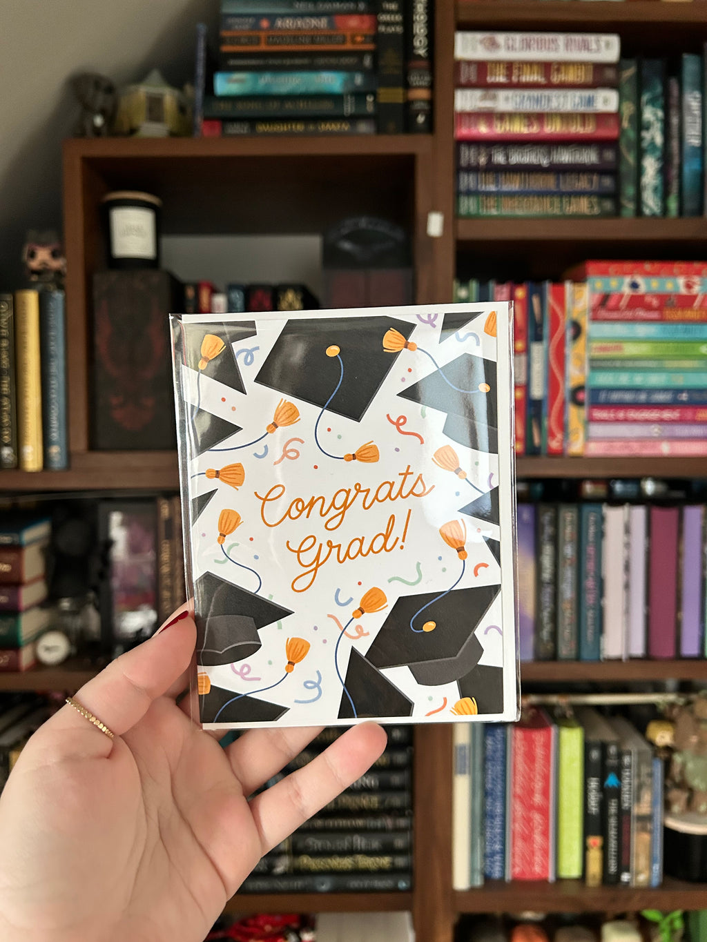 Graduation greeting card featuring black graduation caps, gold tassels, colorful confetti, and the words "Congrats Grad!" on a white background.