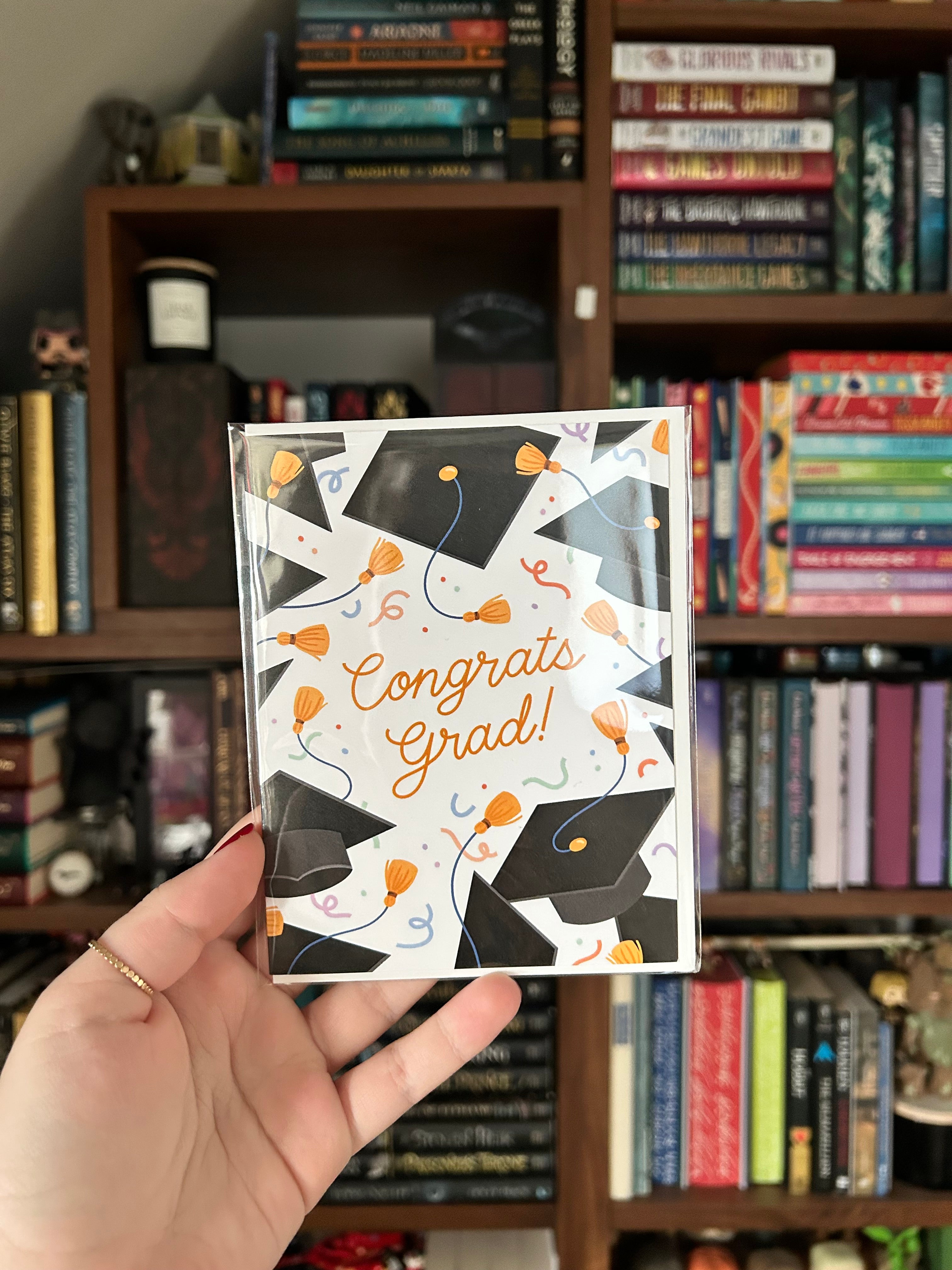 Graduation greeting card featuring black graduation caps, gold tassels, colorful confetti, and the words "Congrats Grad!" on a white background.