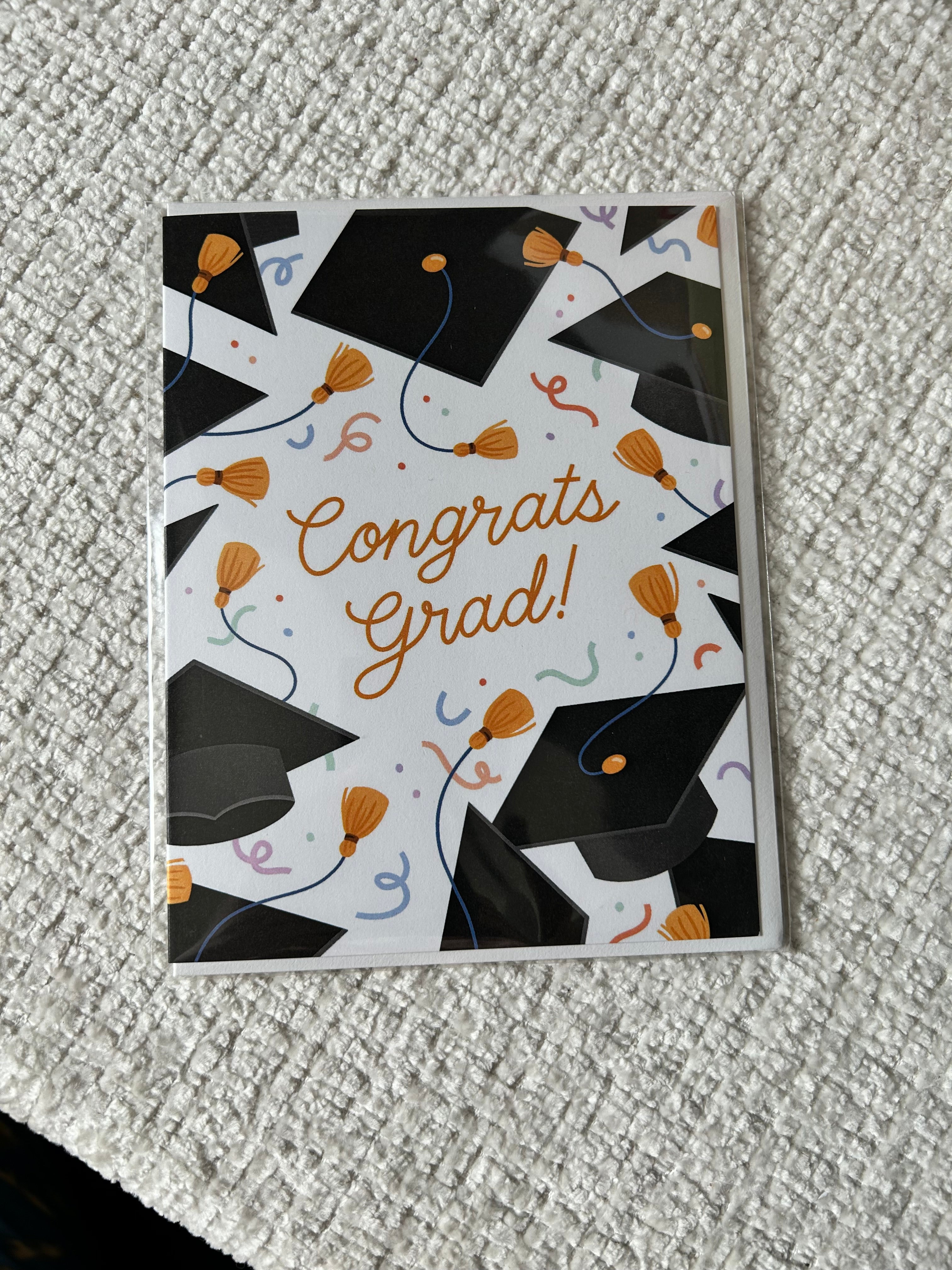 Graduation greeting card featuring black graduation caps, gold tassels, colorful confetti, and the words "Congrats Grad!" on a white background.