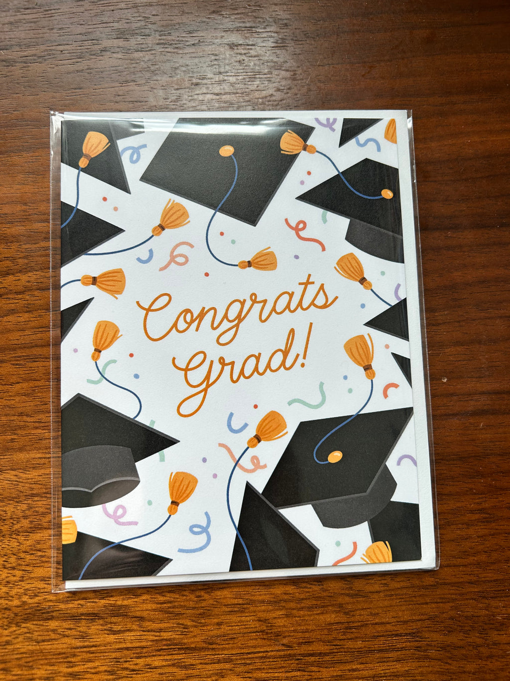 Graduation greeting card featuring black graduation caps, gold tassels, colorful confetti, and the words "Congrats Grad!" on a white background.