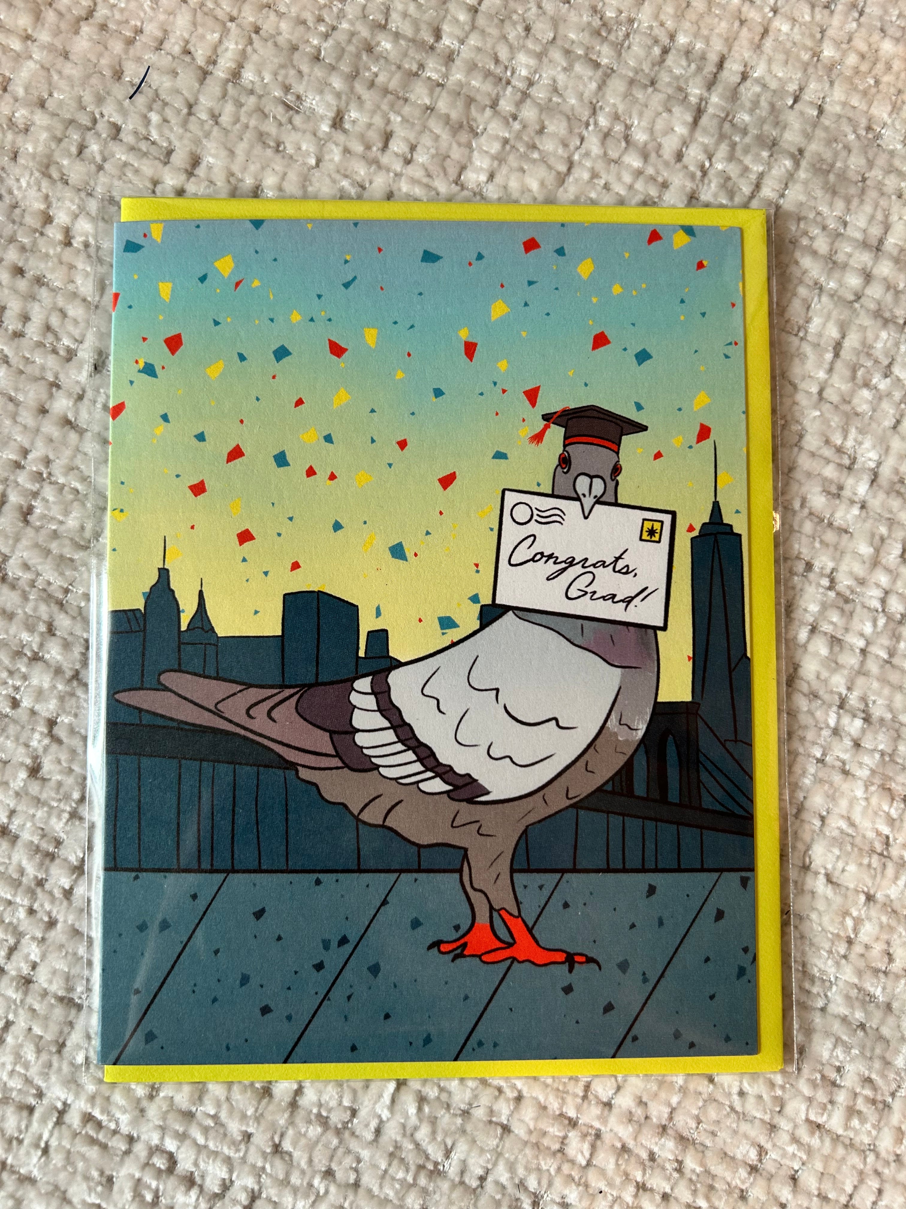 Graduation greeting card featuring a pigeon wearing a graduation cap while delivering a "Congrats, Grad!" letter with the New York City skyline in the background.