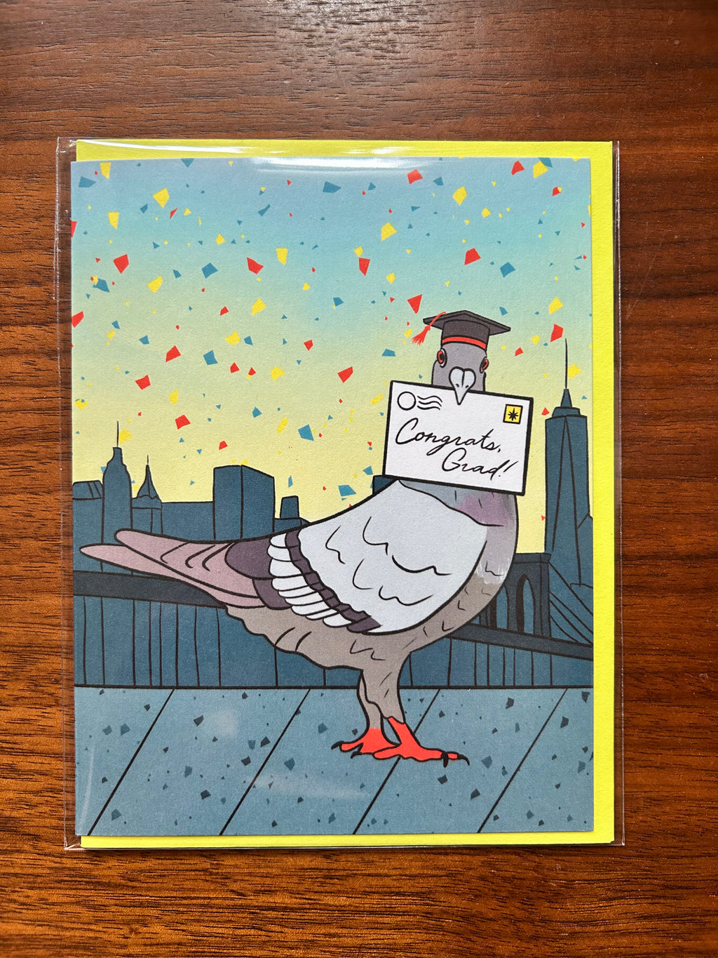 Graduation greeting card featuring a pigeon wearing a graduation cap while delivering a "Congrats, Grad!" letter with the New York City skyline in the background.