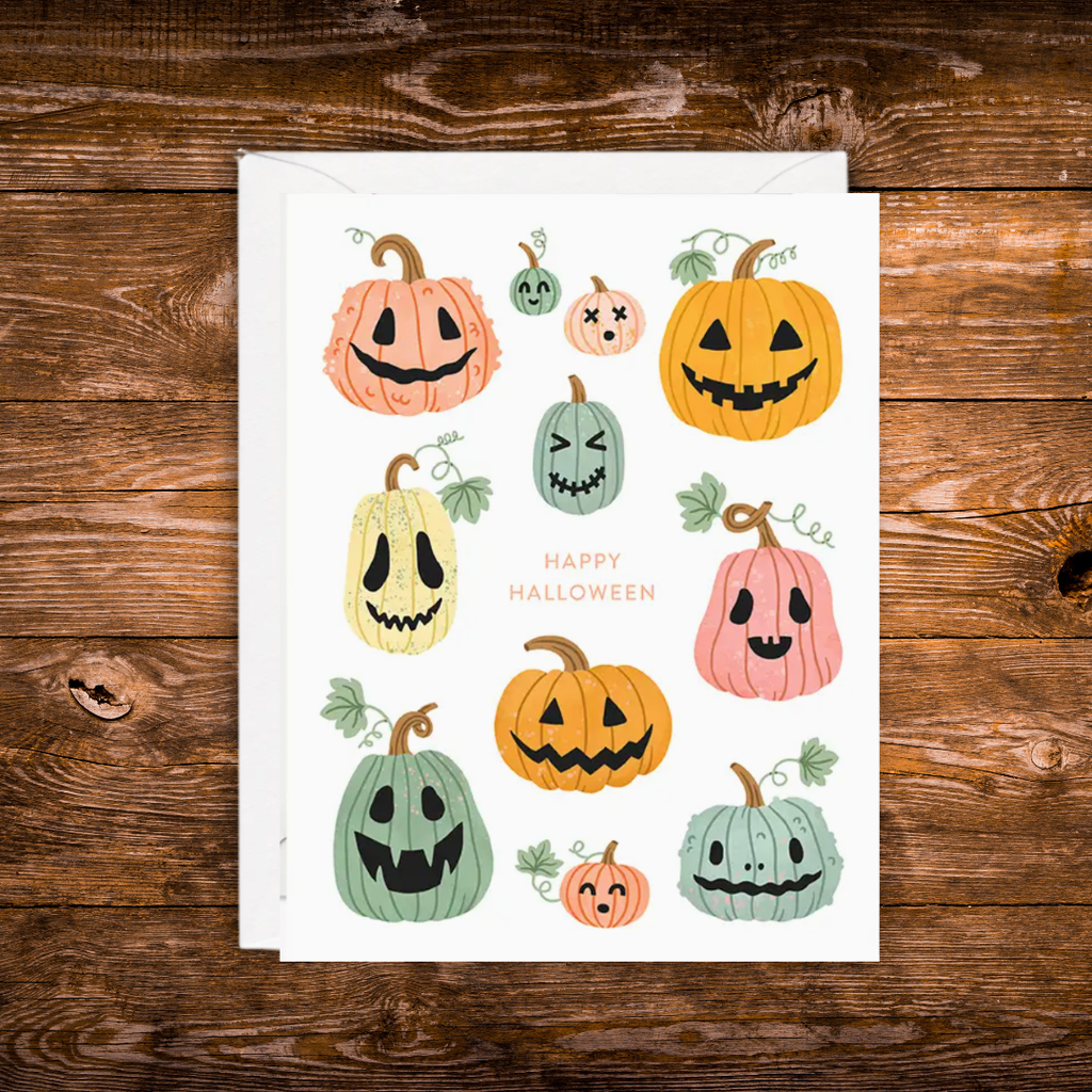 Halloween greeting card featuring colorful smiling jack-o'-lantern pumpkins surrounding the words "Happy Halloween" on a white background with a white envelope.