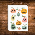 Halloween greeting card featuring colorful smiling jack-o'-lantern pumpkins surrounding the words "Happy Halloween" on a white background with a white envelope.