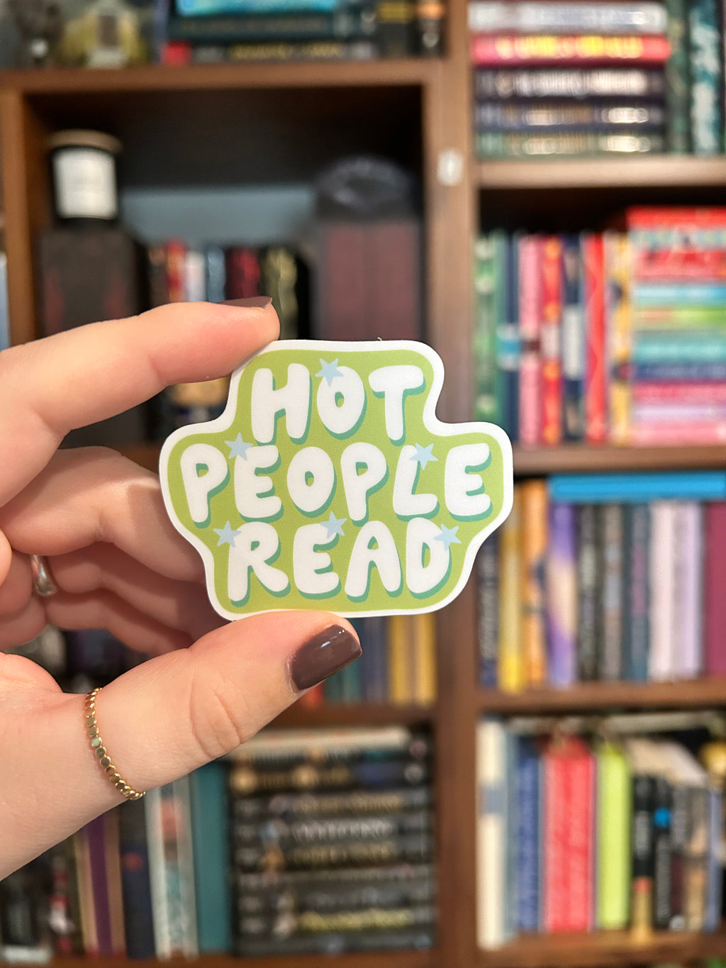 A die-cut sticker with the phrase 'HOT PEOPLE READ' in white bubble letters on a light green background with small blue star accents