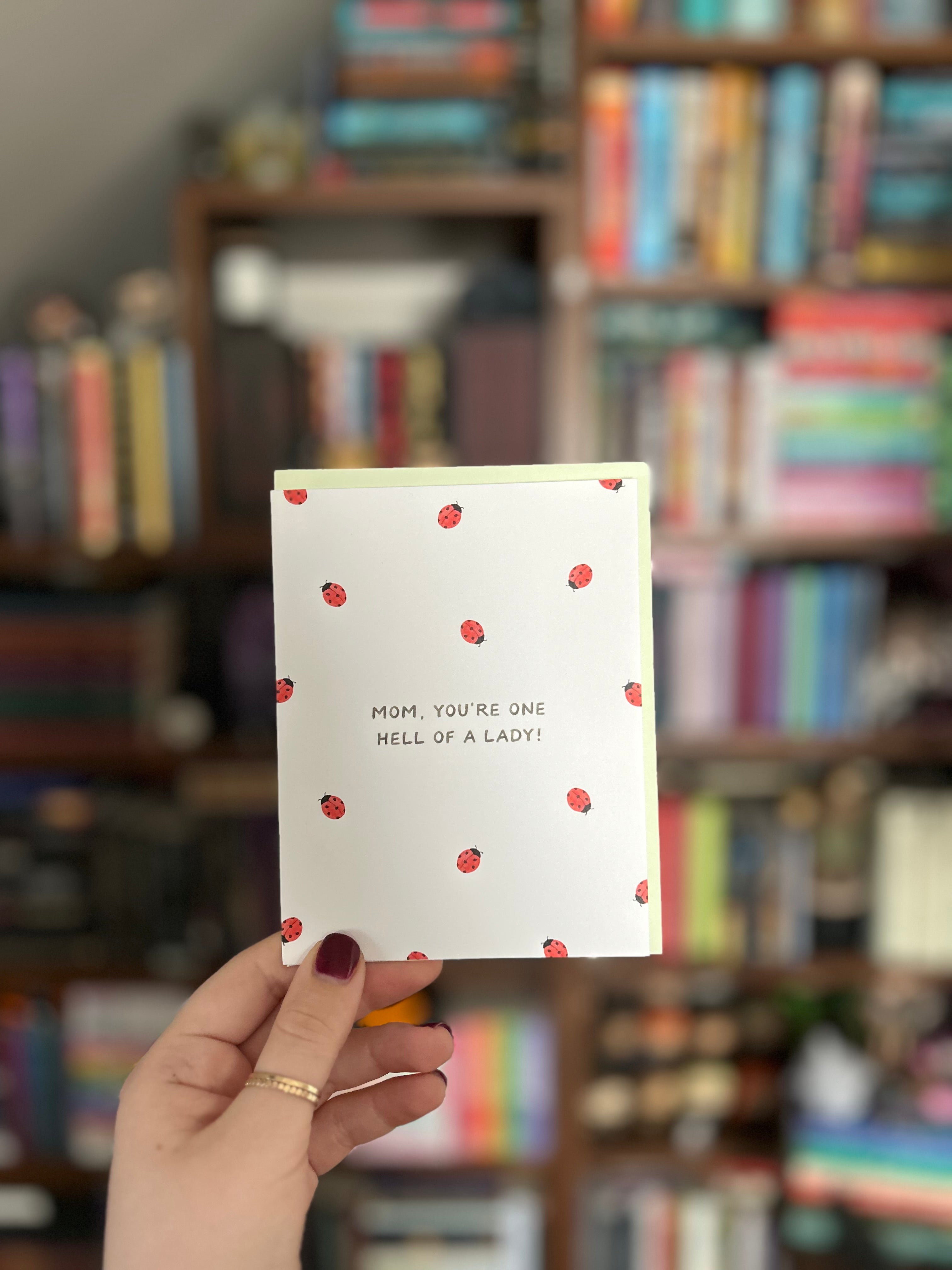 Funny Mother's Day greeting card featuring scattered ladybugs and the message "Mom, You're One Hell of a Lady!" on a white background.