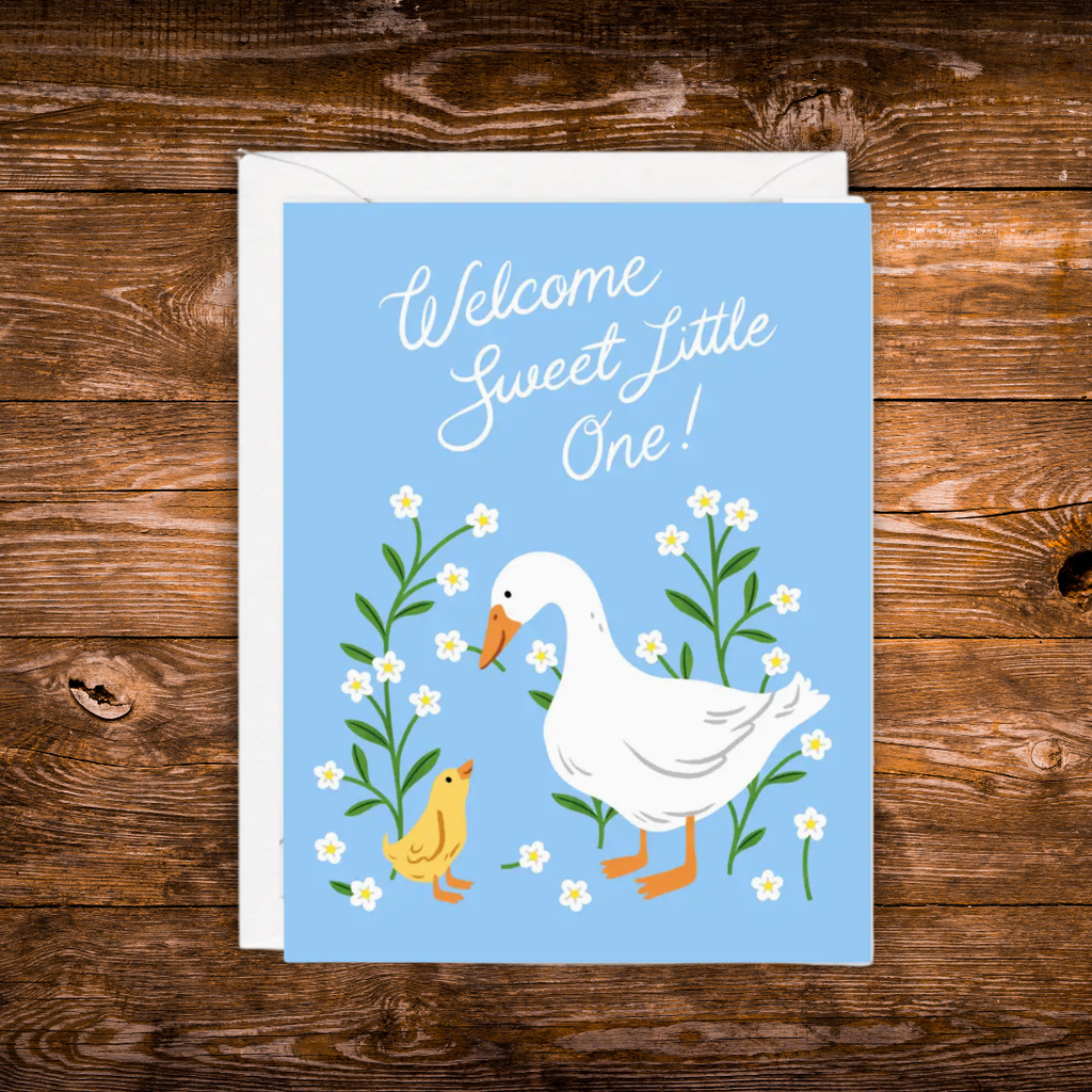 Gender-neutral baby greeting card featuring a white goose and yellow gosling surrounded by white wildflowers on a soft blue background with the message "Welcome Sweet Little One!"