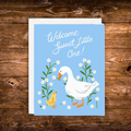 Gender-neutral baby greeting card featuring a white goose and yellow gosling surrounded by white wildflowers on a soft blue background with the message "Welcome Sweet Little One!"