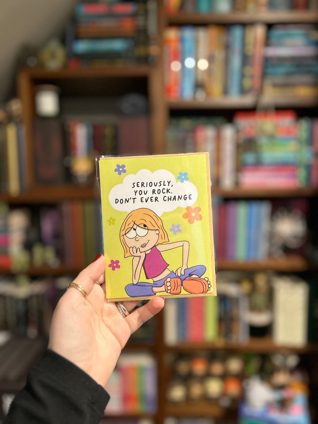 Funny friendship greeting card featuring an illustrated girl sitting with colorful flowers and the message "Seriously, You Rock. Don't Ever Change."