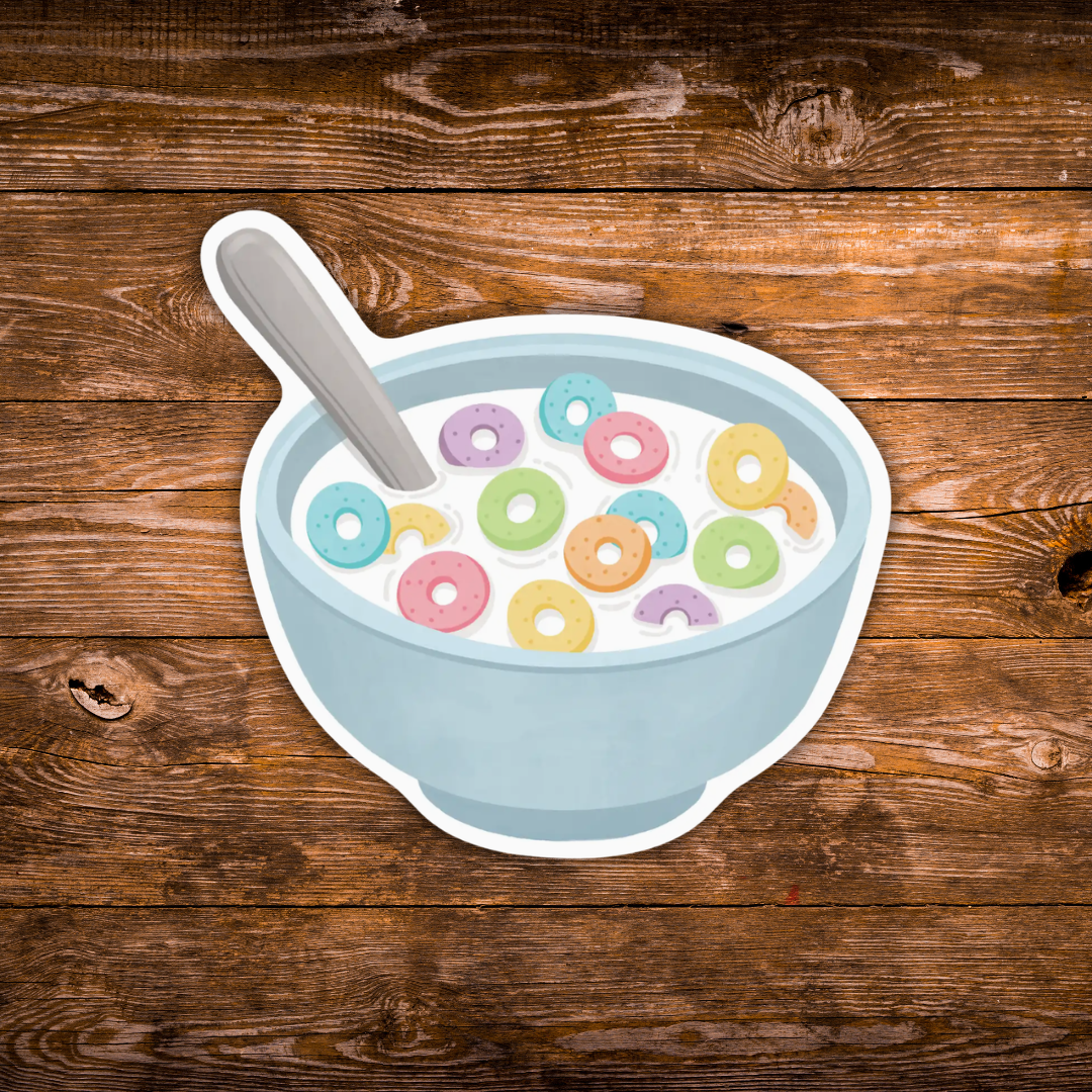 A die-cut sticker depicting a light blue bowl of cereal with colorful ring-shaped cornflakes and a gray spoon, placed on a brown wooden plank background.