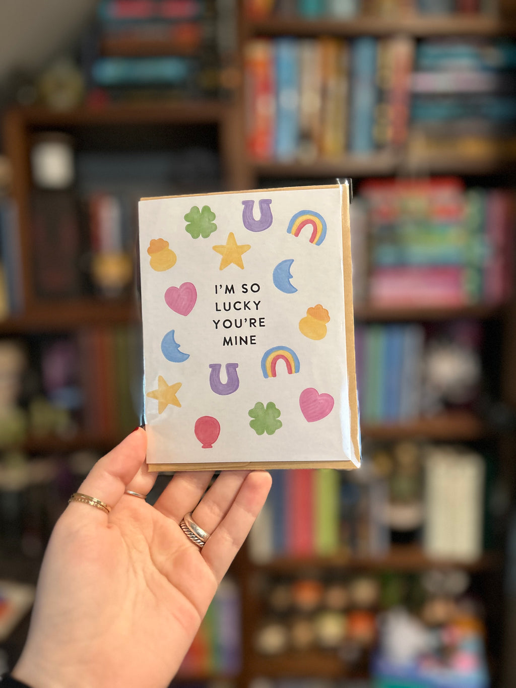 Cute romantic greeting card featuring colorful lucky charms including four-leaf clovers, horseshoes, rainbows, stars, hearts, and moons surrounding the message "I'm So Lucky You're Mine."