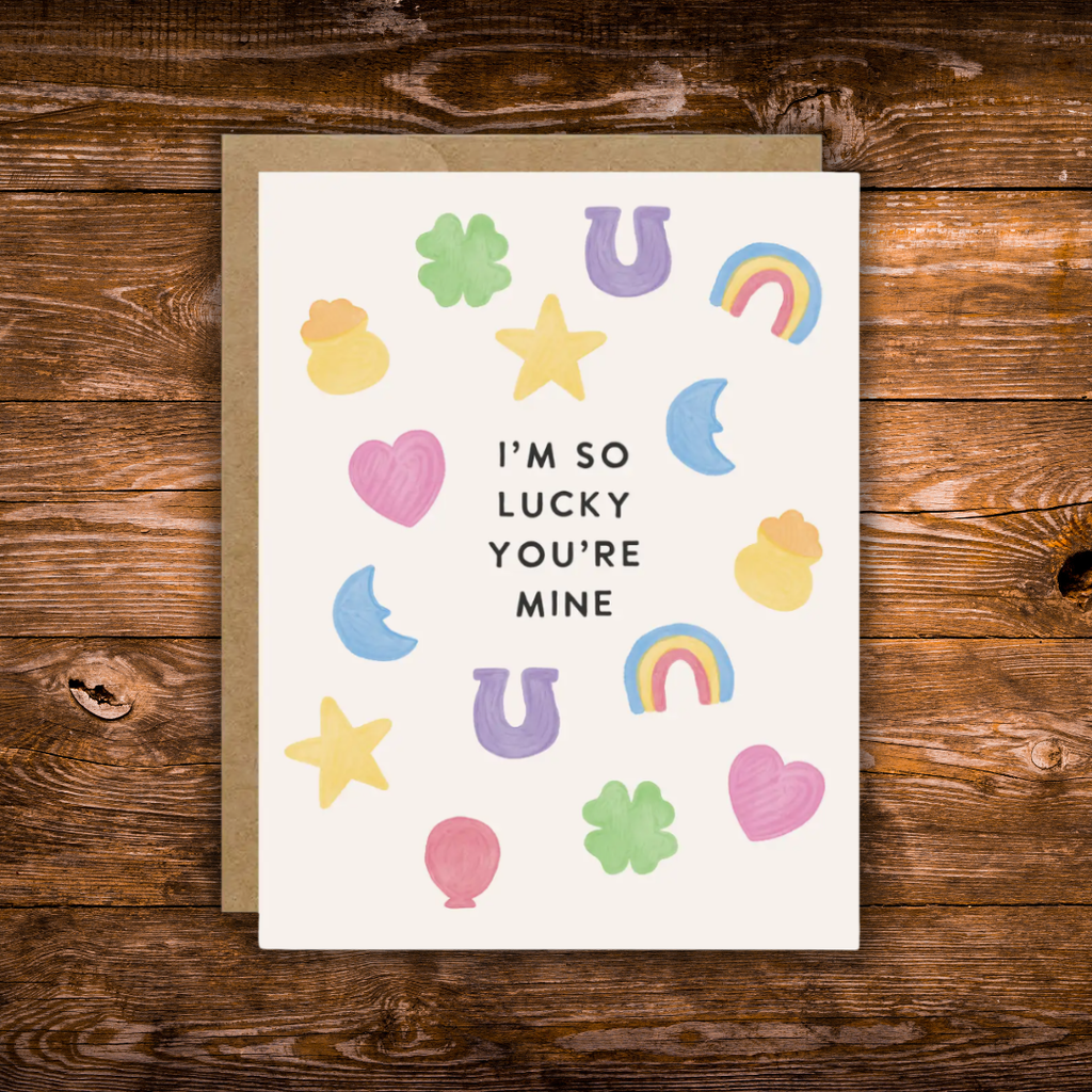 Cute romantic greeting card featuring colorful lucky charms including four-leaf clovers, horseshoes, rainbows, stars, hearts, and moons surrounding the message "I'm So Lucky You're Mine."