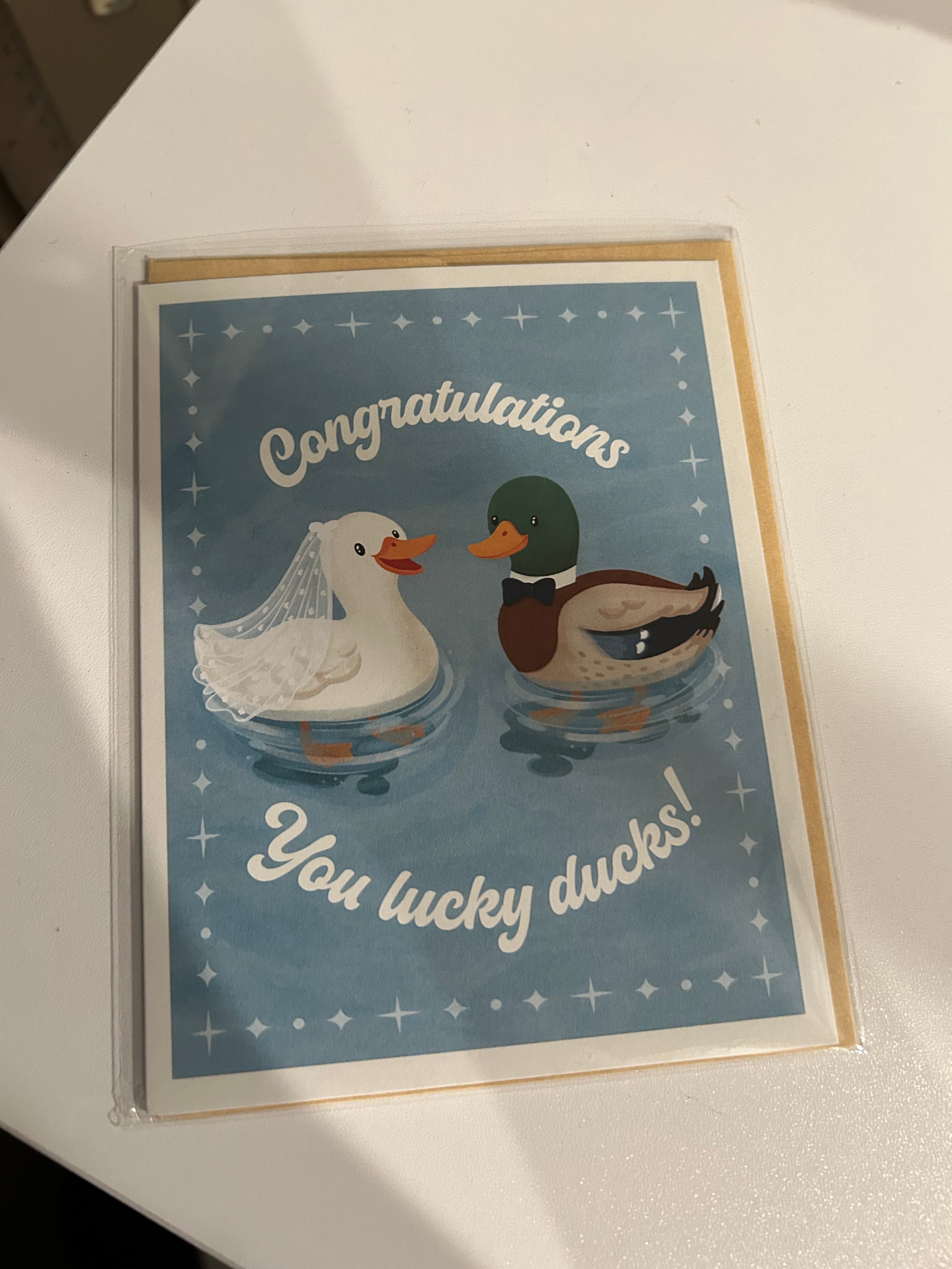 Wedding congratulations greeting card featuring a bride duck wearing a veil and a groom duck wearing a bow tie with the phrase "Congratulations You Lucky Ducks!"