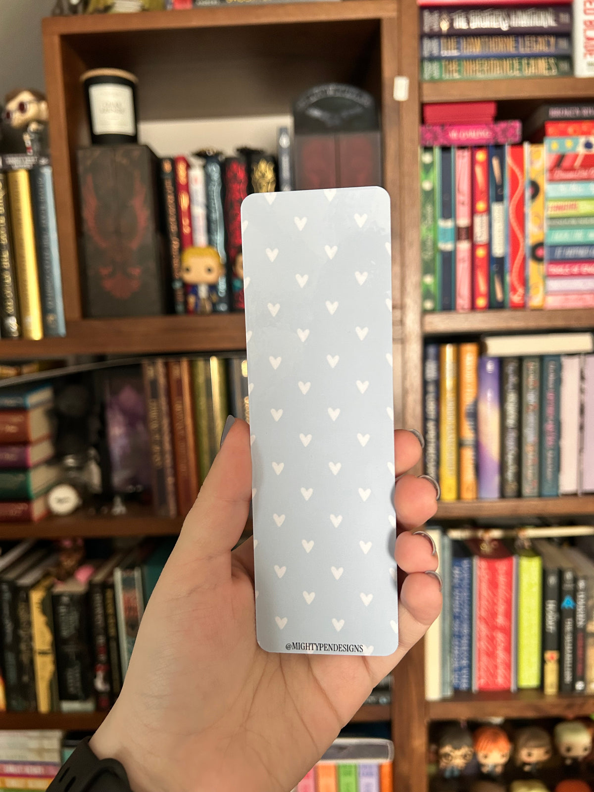 Double-sided mallard duck bookmark featuring a green-headed duck holding a tiny knife beneath the words “You better finish this one,” standing in a daisy meadow, with a white heart pattern on a light blue reverse.