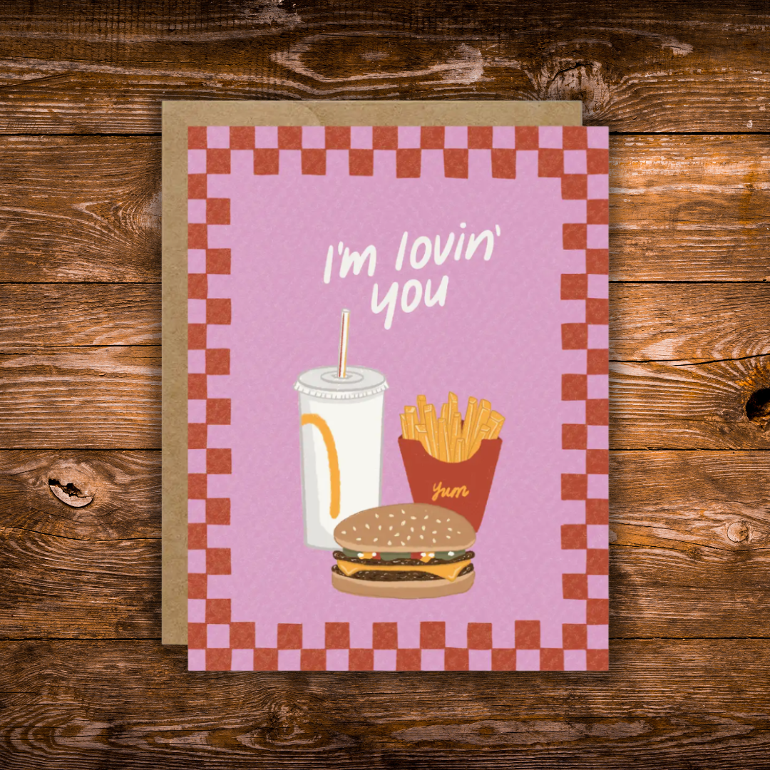 Cute romantic greeting card featuring an illustrated burger, fries, and soda with the message "I'm Lovin' You" on a retro pink background with a checkerboard border.