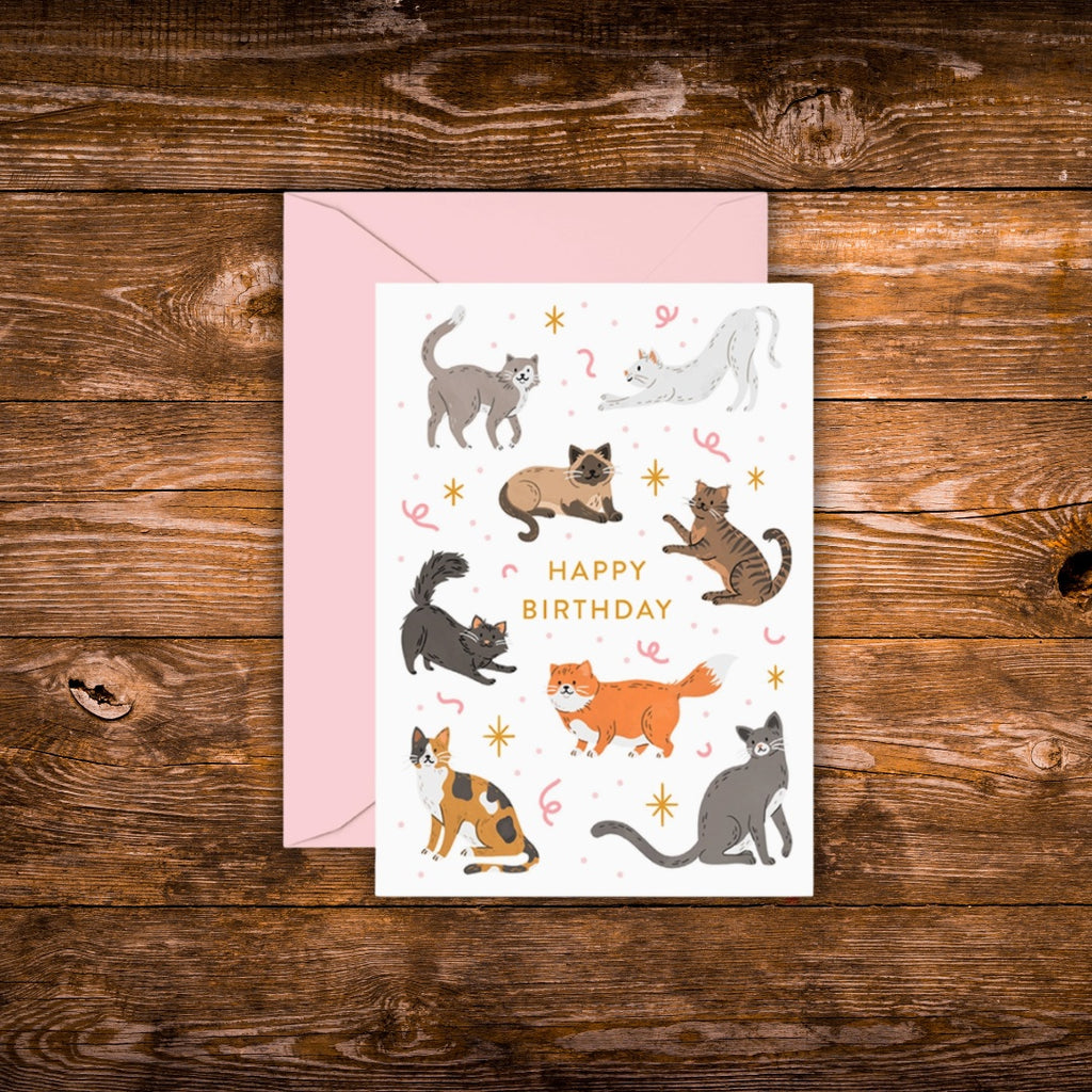 Mini birthday greeting card featuring playful illustrated cats surrounding the words "Happy Birthday" on a white background with a pink envelope.