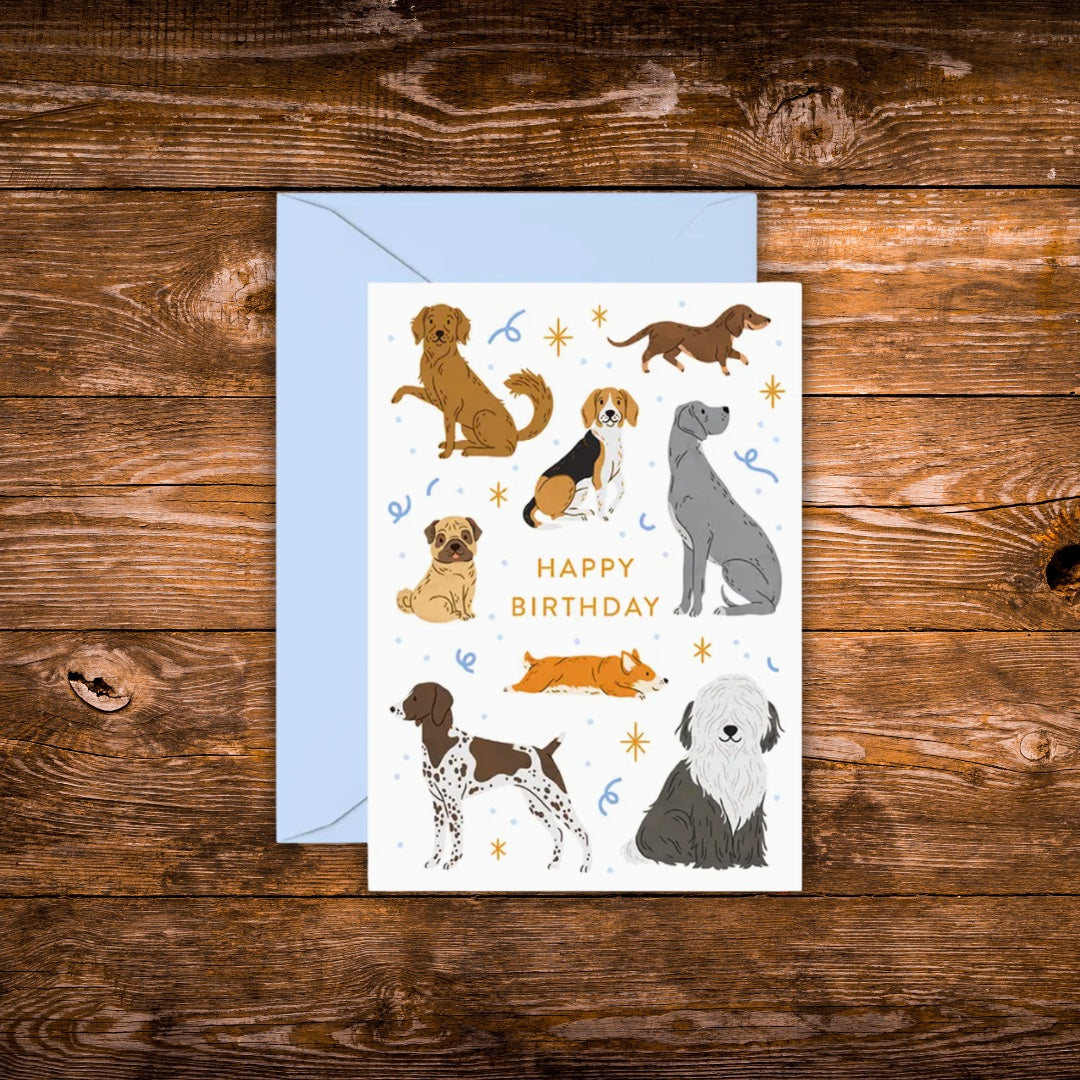 Mini birthday greeting card featuring illustrated dogs of various breeds surrounding the words "Happy Birthday" on a white background with a light blue envelope.
