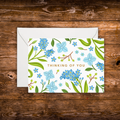 Mini landscape greeting card featuring blue floral illustrations surrounding the words "Thinking of You" on a white background.