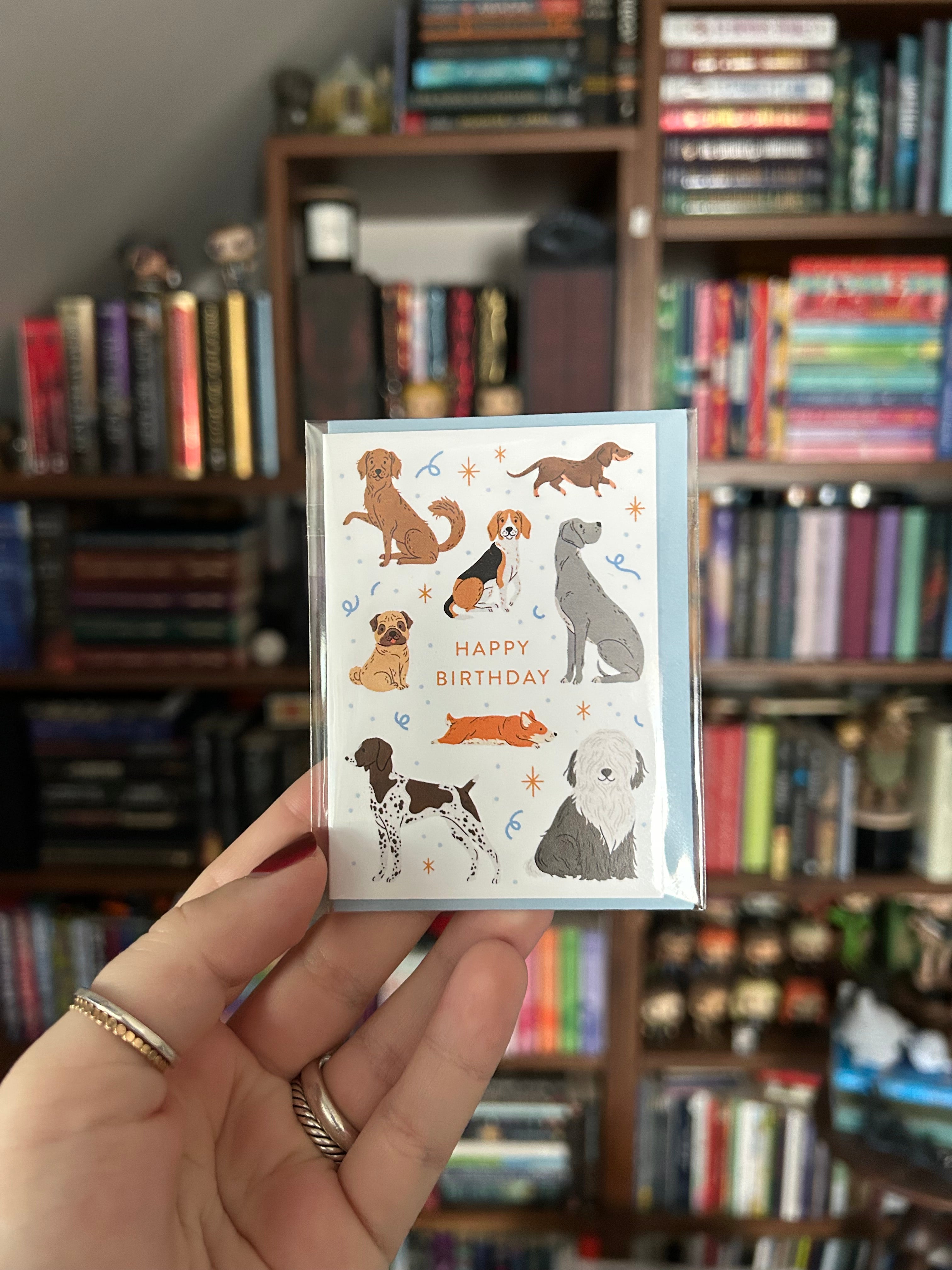 Mini birthday greeting card featuring illustrated dogs of various breeds surrounding the words "Happy Birthday" on a white background with a light blue envelope.