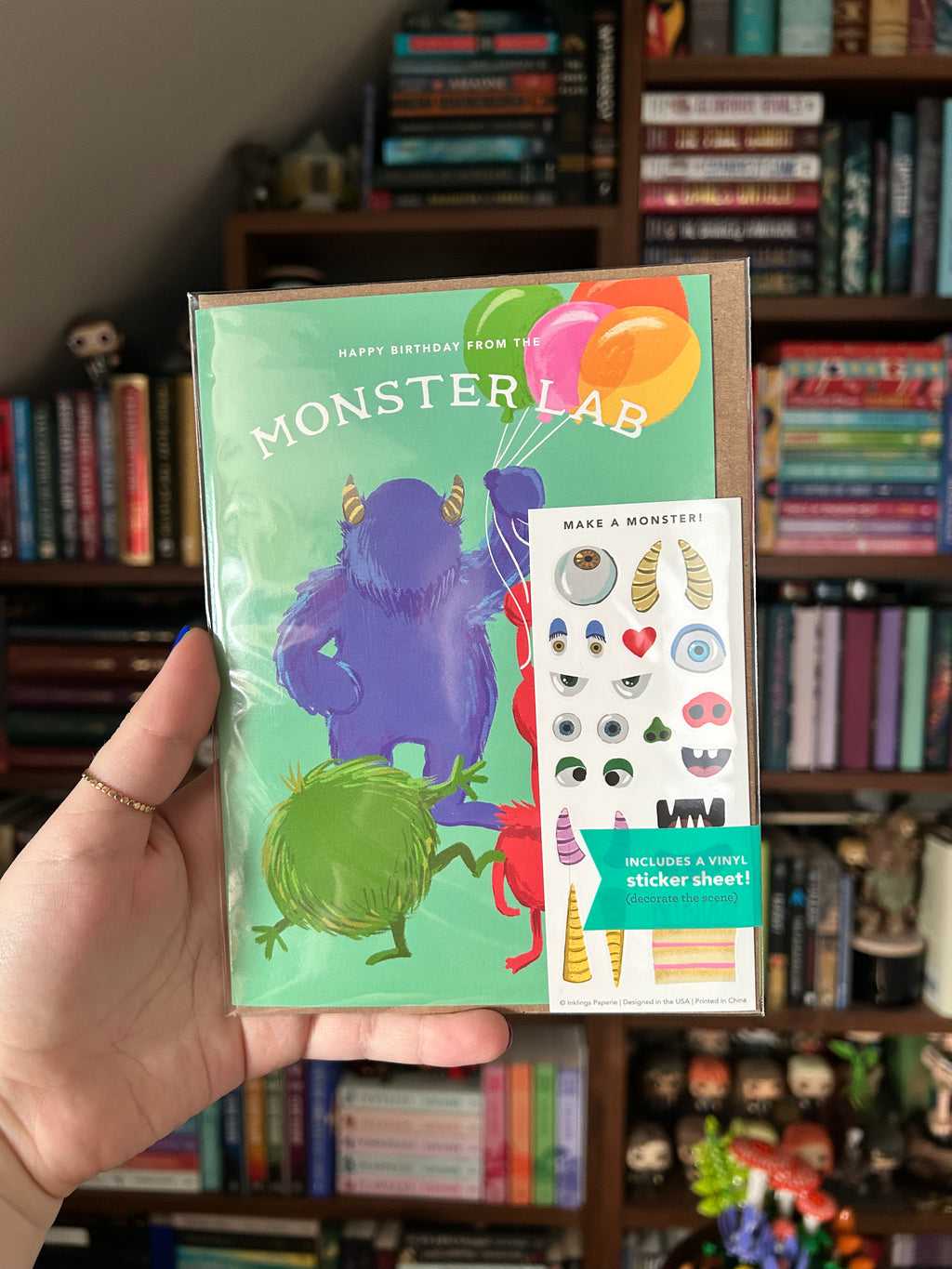 Interactive monster birthday greeting card featuring cute colorful monsters holding balloons with a matching "Make a Monster" sticker sheet for creating silly monster faces.