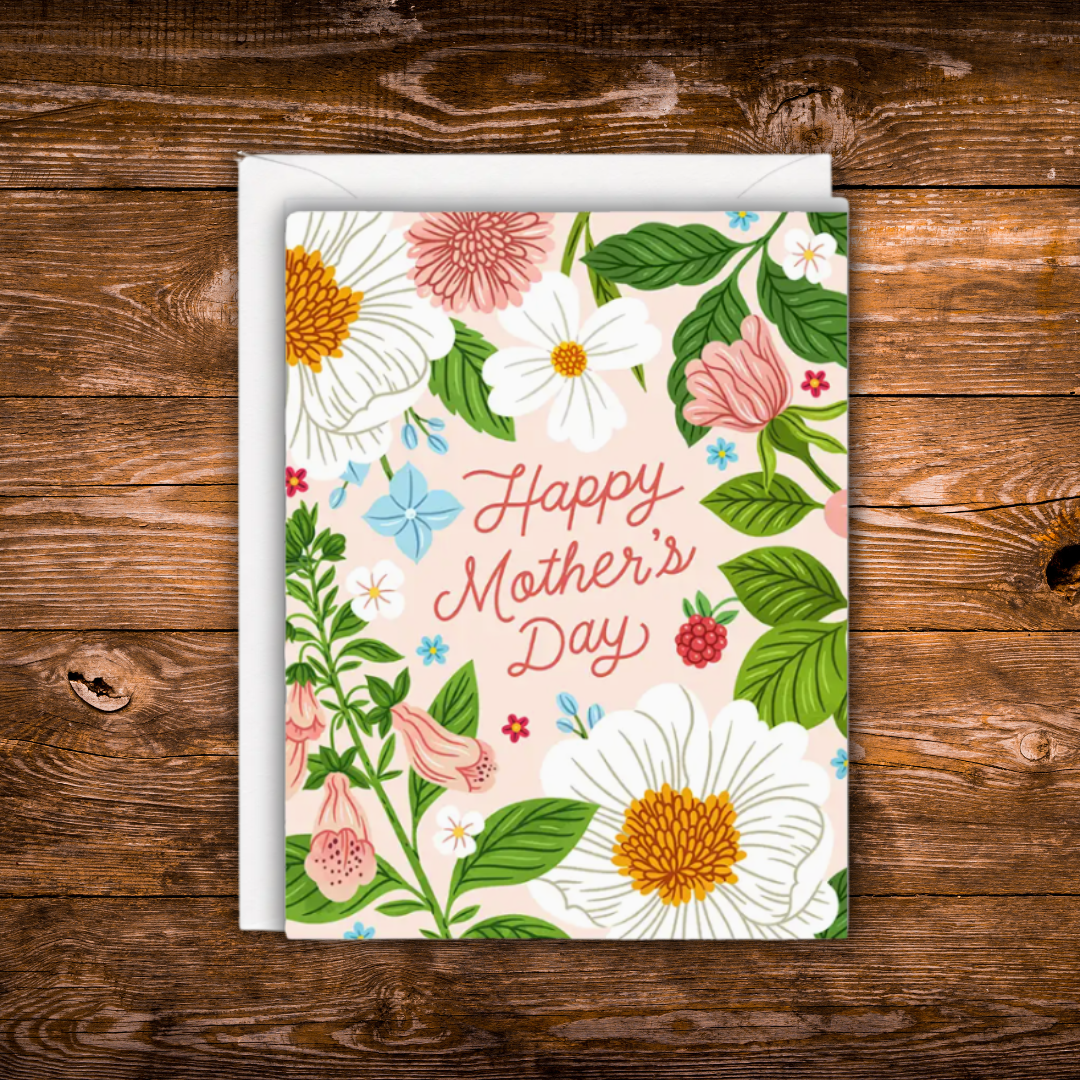 Mother's Day greeting card featuring colorful spring flowers surrounding the words "Happy Mother's Day" on a soft blush background.