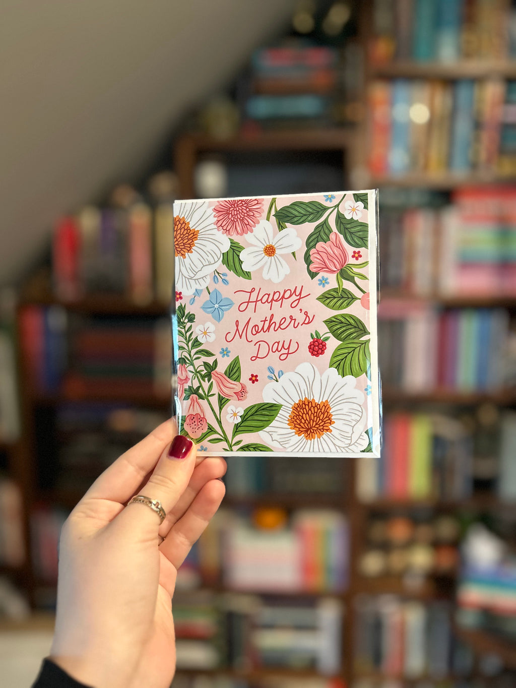 Mother's Day greeting card featuring colorful spring flowers surrounding the words "Happy Mother's Day" on a soft blush background.