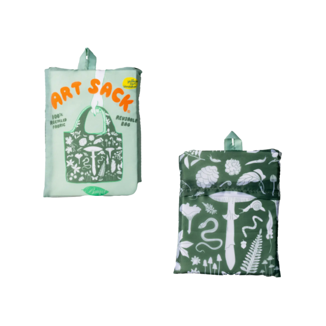 Reusable tote bag shown folded, with the front and back sides visible. The front features a pale mint-green background with orange “ART SACK” lettering and a dark green botanical illustration of mushrooms, flowers, leaves, and other nature motifs. The back features the same dark green nature-inspired pattern with mushrooms, flowers, leaves, ferns, and a large central mushroom illustration.