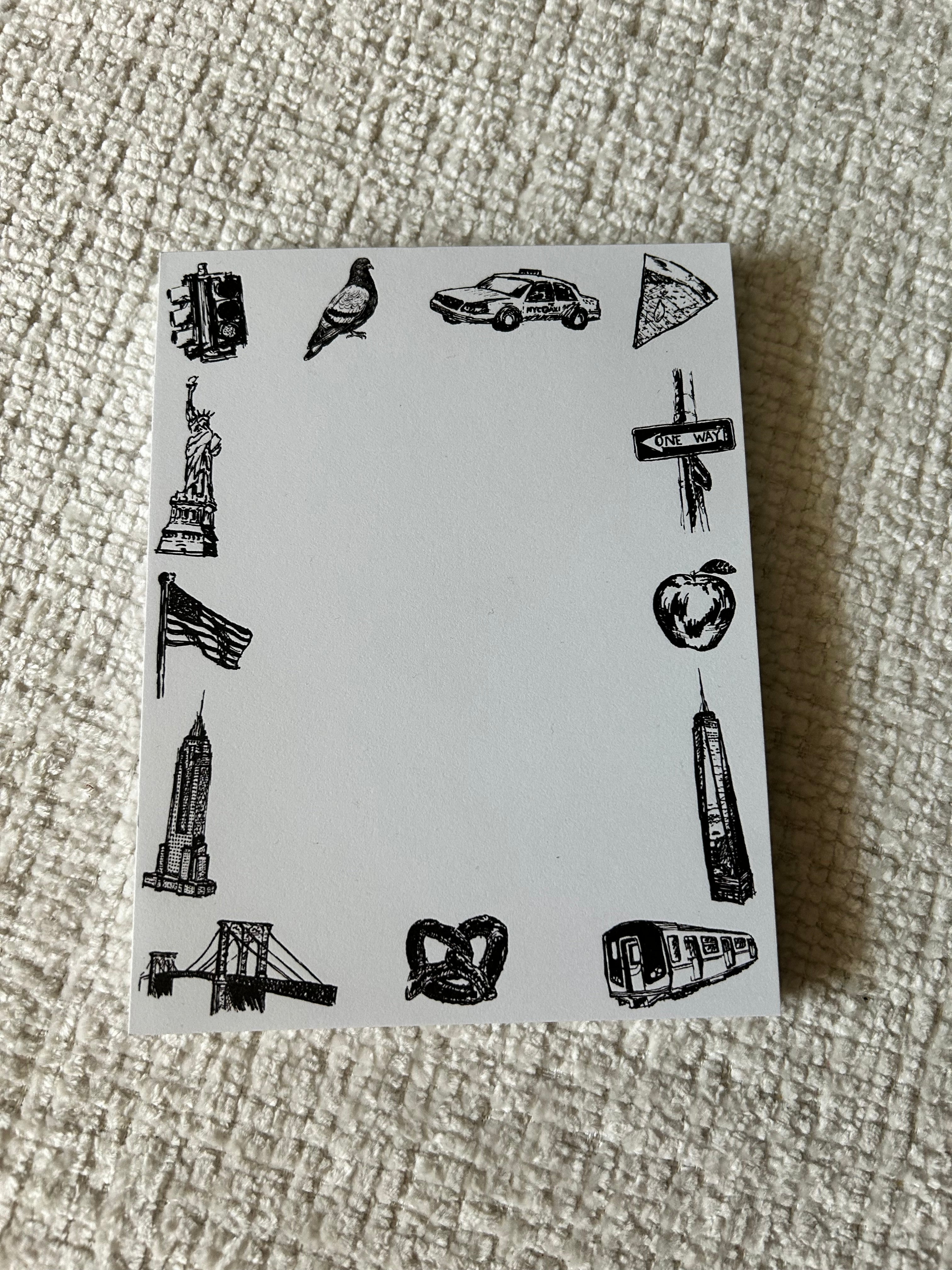 Illustrated New York City tear-away notepad featuring hand-drawn NYC landmarks and icons including the Statue of Liberty, Empire State Building, subway train, taxi, pizza, pigeon, and pretzel surrounding a blank writing area.