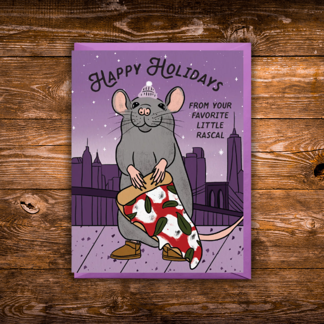 A rectangular holiday greeting card featuring an illustrated gray rat wearing a small white hat and holding a red-and-white patterned gift bag, with the text 'Happy Holidays' and 'From Your Favorite Little Rascal.' The card is photographed flat on a rustic brown wood surface.
