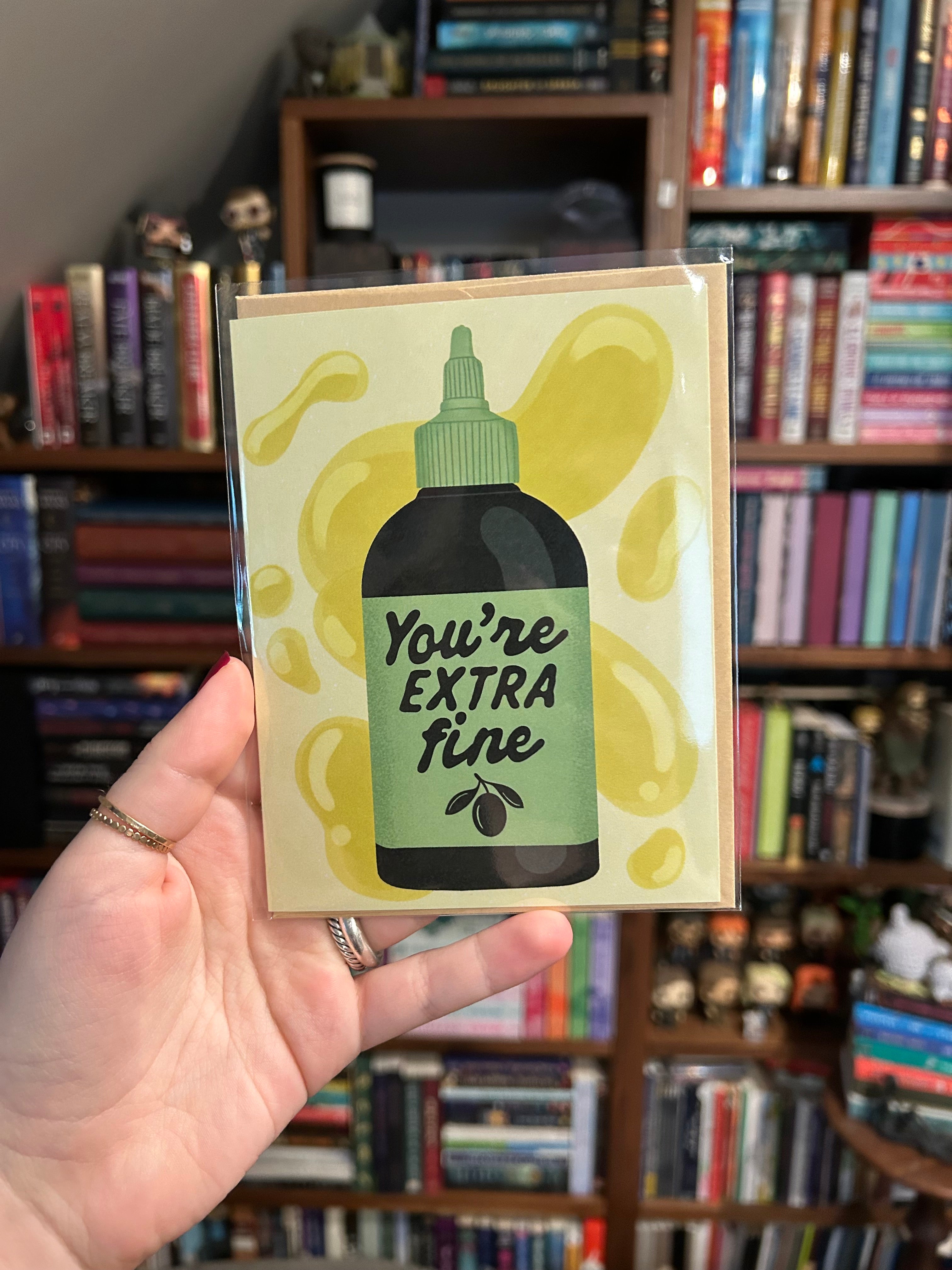 Funny greeting card featuring an olive oil bottle with the phrase "You're Extra Fine" on a light yellow background with olive oil splashes.