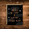 Funny birthday greeting card featuring colorful hand-lettered text reading "Older, Wiser & Hotter Than Ever" on a black background with modern celestial accents.