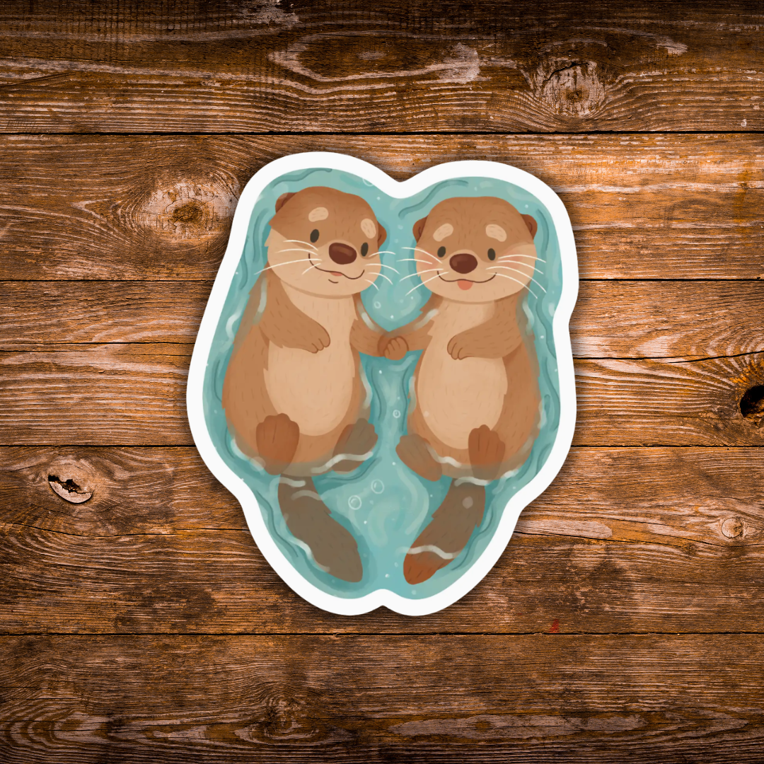A die-cut sticker featuring a cartoon illustration of two smiling brown otters floating in light blue water, shown on a rustic brown wooden plank background.