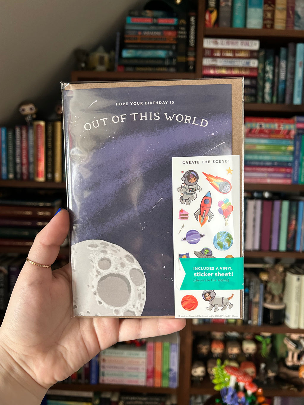 Interactive space birthday greeting card featuring a moon, starry night sky, and "Hope Your Birthday is Out of This World" with a matching space-themed sticker sheet including astronauts, rockets, planets, and aliens.