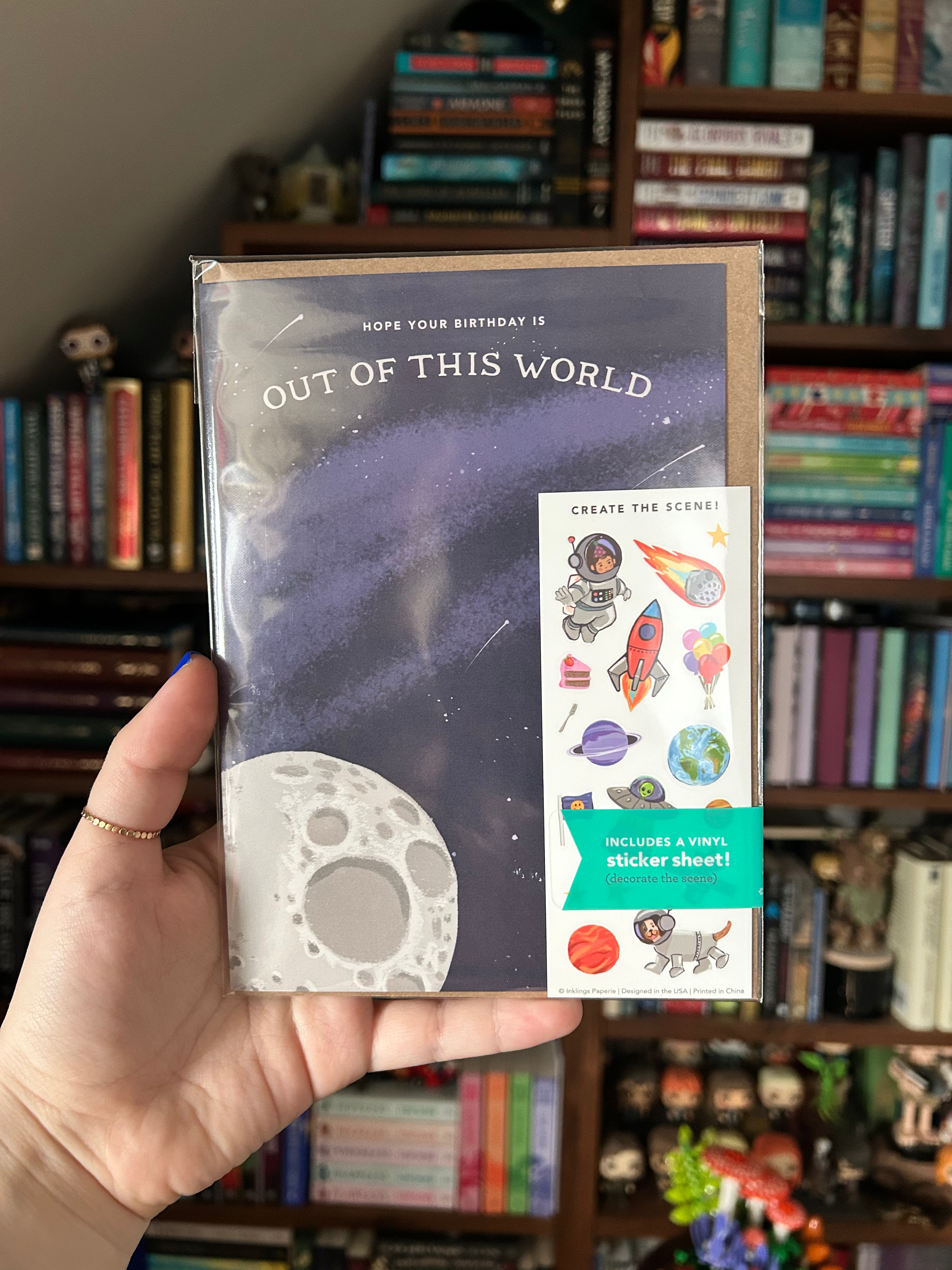 Interactive space birthday greeting card featuring a moon, starry night sky, and "Hope Your Birthday is Out of This World" with a matching space-themed sticker sheet including astronauts, rockets, planets, and aliens.