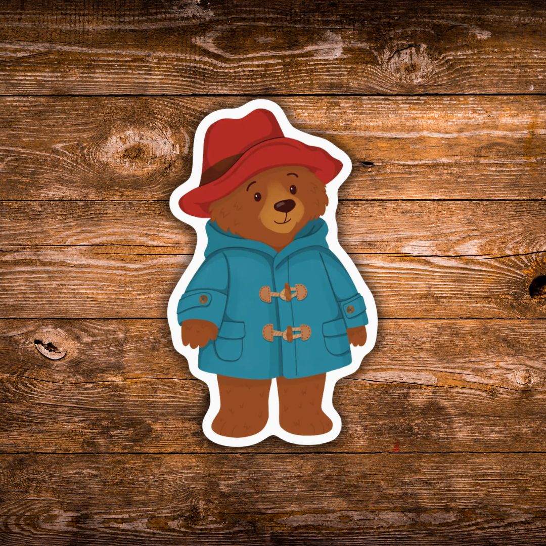 A die-cut sticker of a Bear character wearing a red hat and blue duffel coat, displayed on a rustic brown wooden plank background.