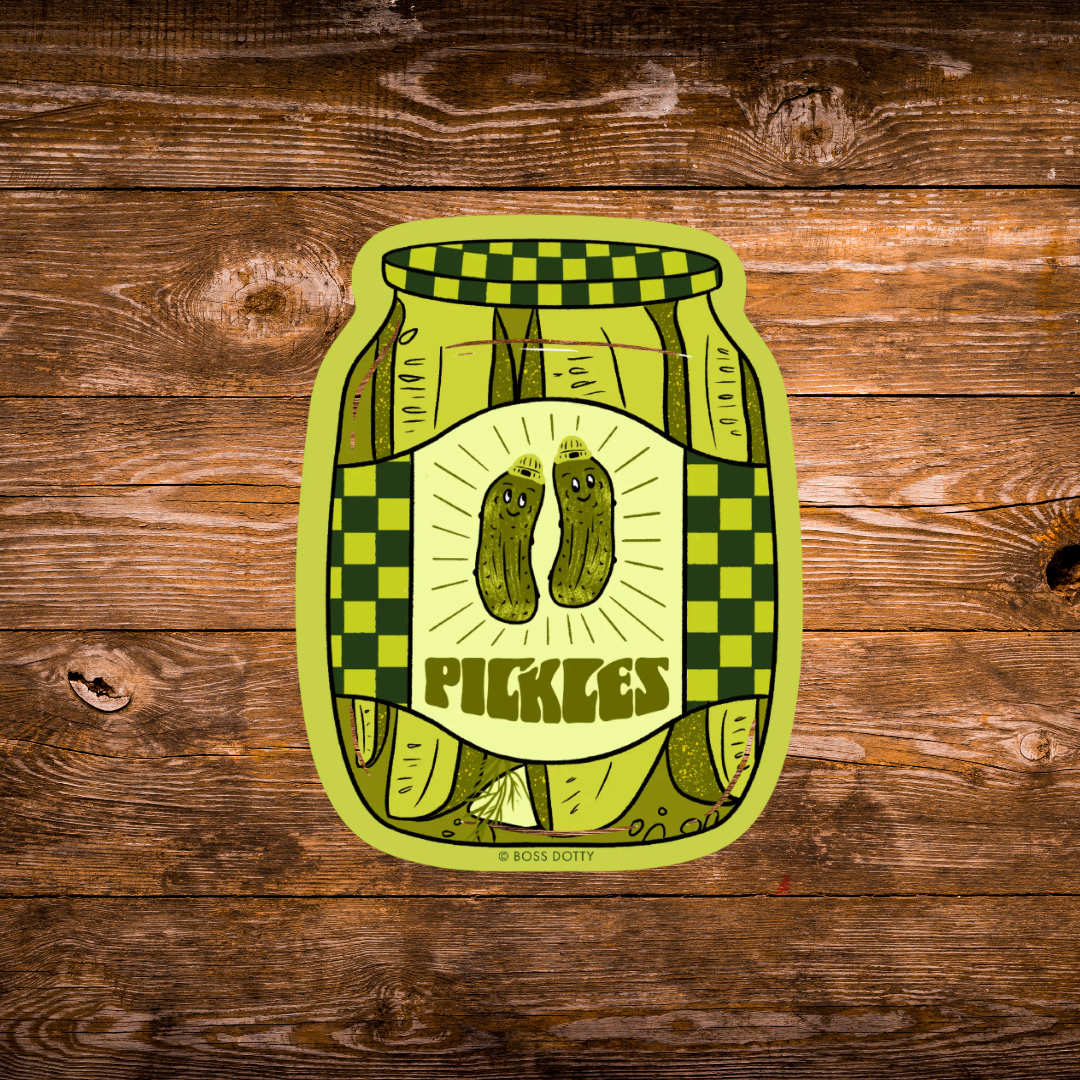 A die-cut sticker featuring a stylized pickle jar illustration with two smiling pickles and the word “PICKLES,” shown on a rustic brown wood plank background. Small text at the bottom reads “© BOSS DOTTY.