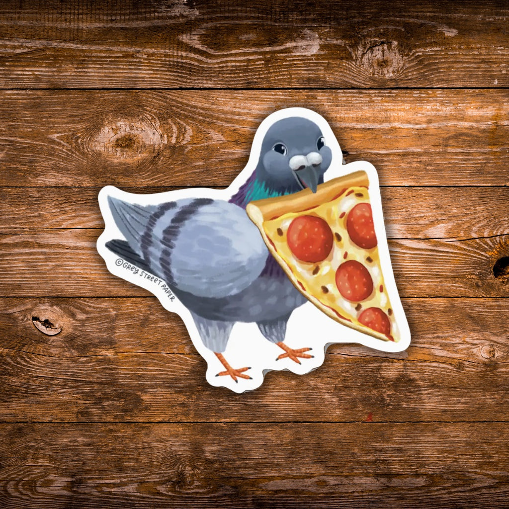 A die-cut sticker featuring an illustration of a gray pigeon holding a slice of pepperoni pizza, placed on a rustic brown wooden surface.