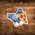 A die-cut sticker featuring an illustration of a gray pigeon holding a slice of pepperoni pizza, placed on a rustic brown wooden surface.