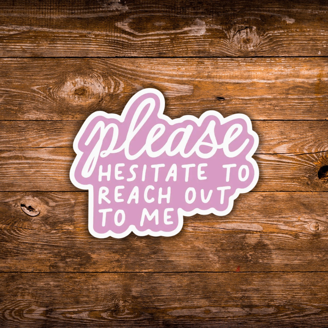 A die-cut sticker with the phrase 'please HESITATE TO REACH OUT TO ME' in white lettering on a pink cloud-like shape, shown on a rustic brown wooden background.