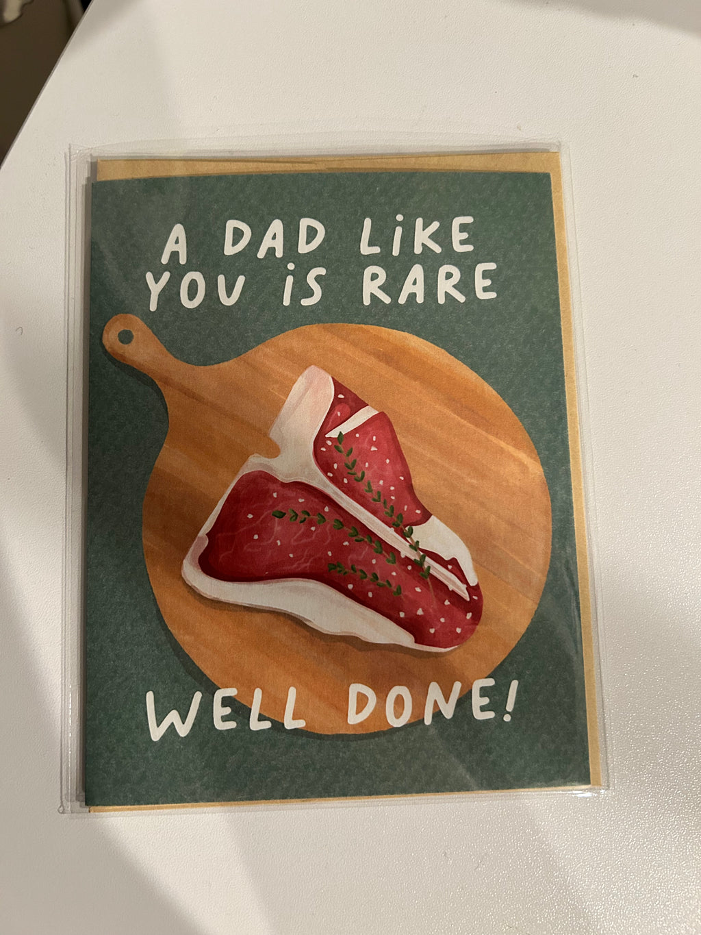 Funny Father's Day greeting card featuring an illustrated steak on a wooden cutting board with the message "A Dad Like You Is Rare. Well Done!"