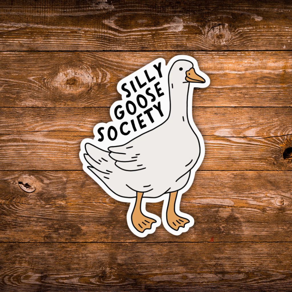 A die-cut sticker featuring a cartoon white goose with orange beak and legs, with the text 'SILLY GOOSE SOCIETY' in black lettering on a curved banner above it. The sticker is displayed flat against a rustic brown wooden plank background.