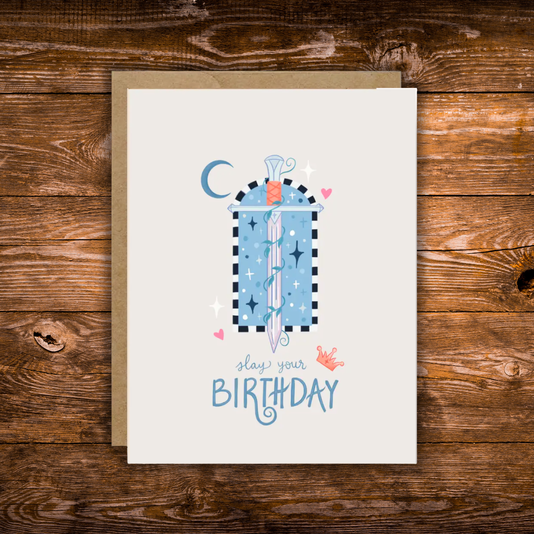 Fantasy-inspired birthday greeting card featuring a magical sword surrounded by stars, hearts, a crescent moon, and the message "Slay Your Birthday" on a soft neutral background.