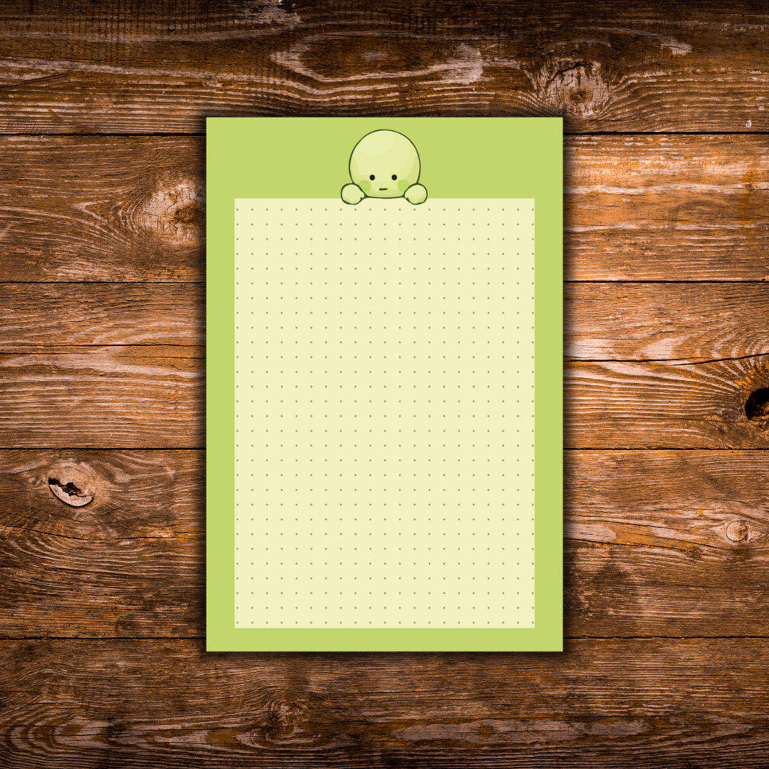 lime-green notepad with a pale green character peeking over the top of a cream dotted writing area, displayed on a rustic wooden background.