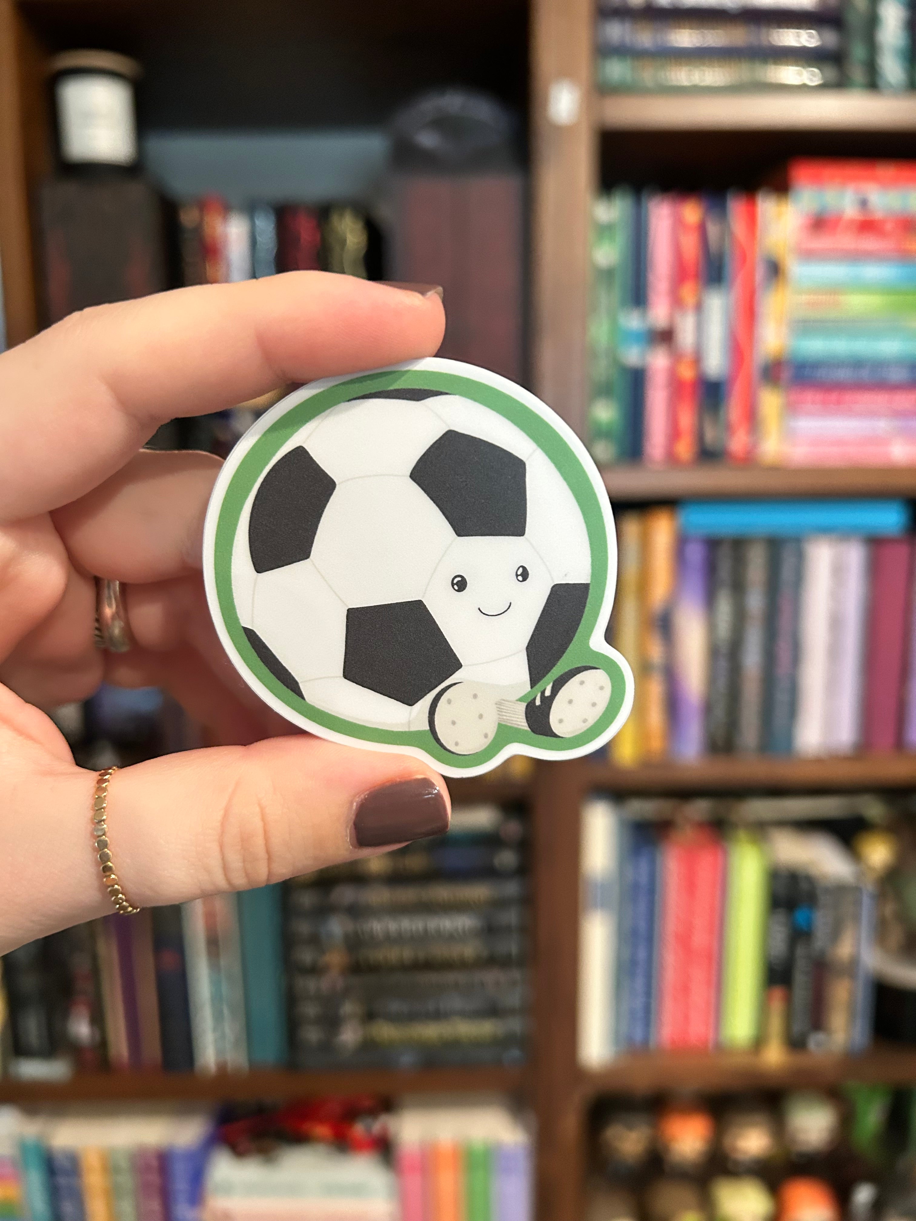 Cute smiling soccer ball sticker with little cleats and a green outline.