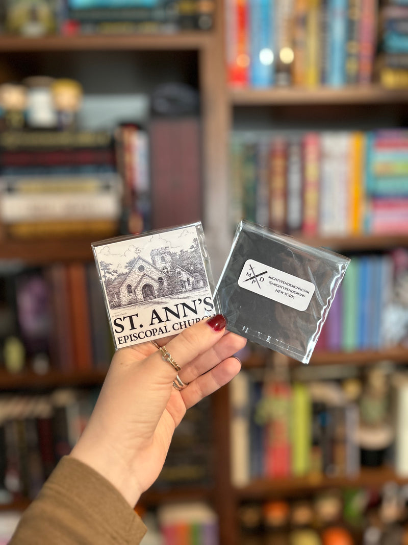 A hand holds two small magnets in front of a blurred bookshelf background. 