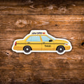 A die-cut vinyl sticker of a yellow New York City taxi cab with black checkered stripes, shown on a rustic brown wooden plank background.