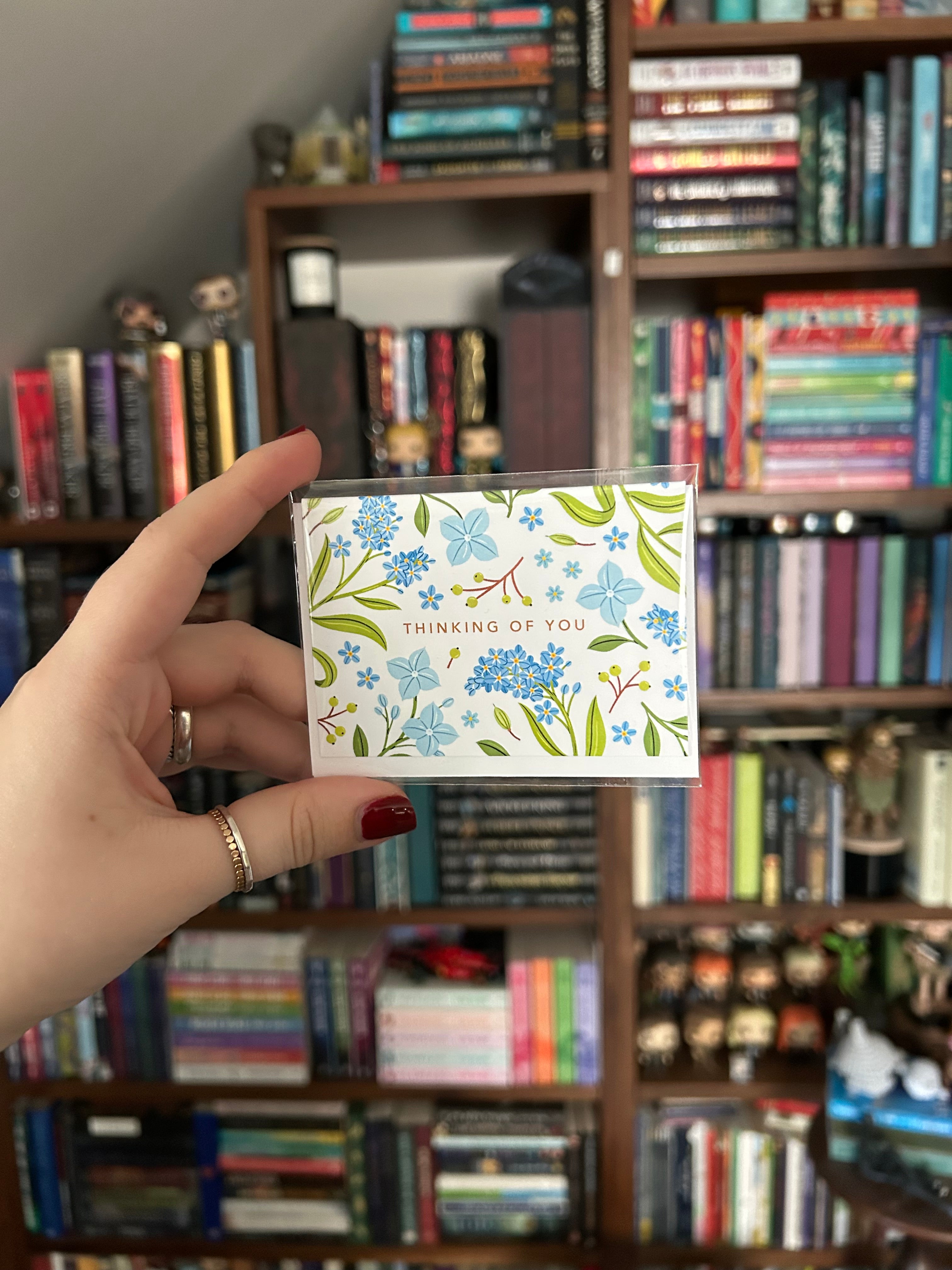 Mini landscape greeting card featuring blue floral illustrations surrounding the words "Thinking of You" on a white background.