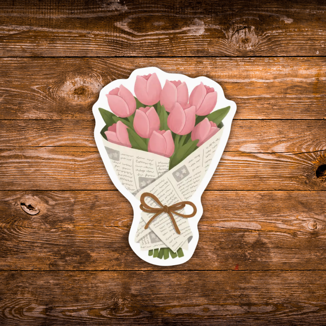 A die-cut sticker depicting a bouquet of pink tulips wrapped in newspaper and tied with a brown bow, shown on a rustic brown wooden background.