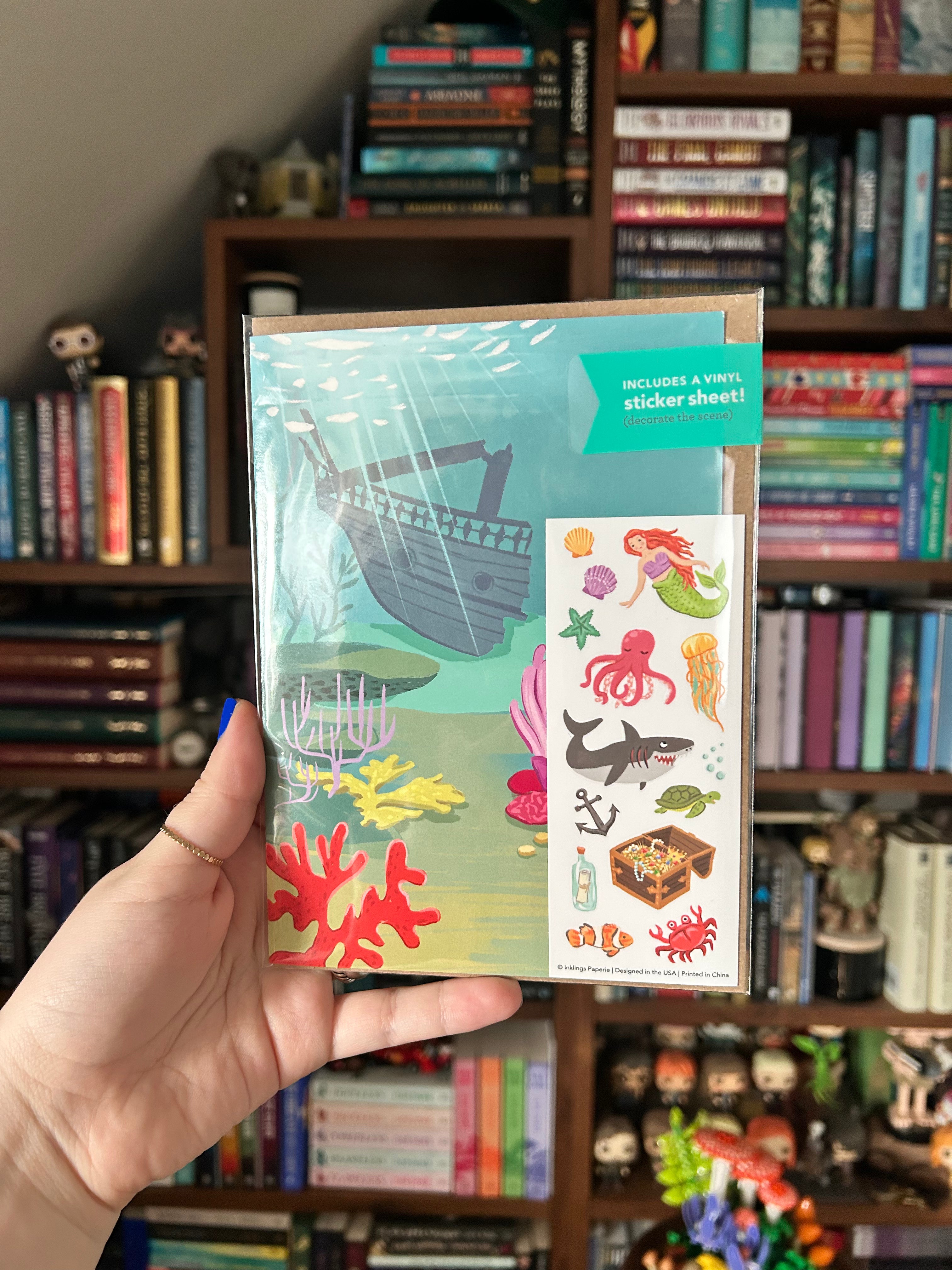 Interactive Under the Sea greeting card featuring an underwater shipwreck scene with a coordinating sticker sheet filled with mermaids, sea creatures, coral, treasure, and ocean accessories.